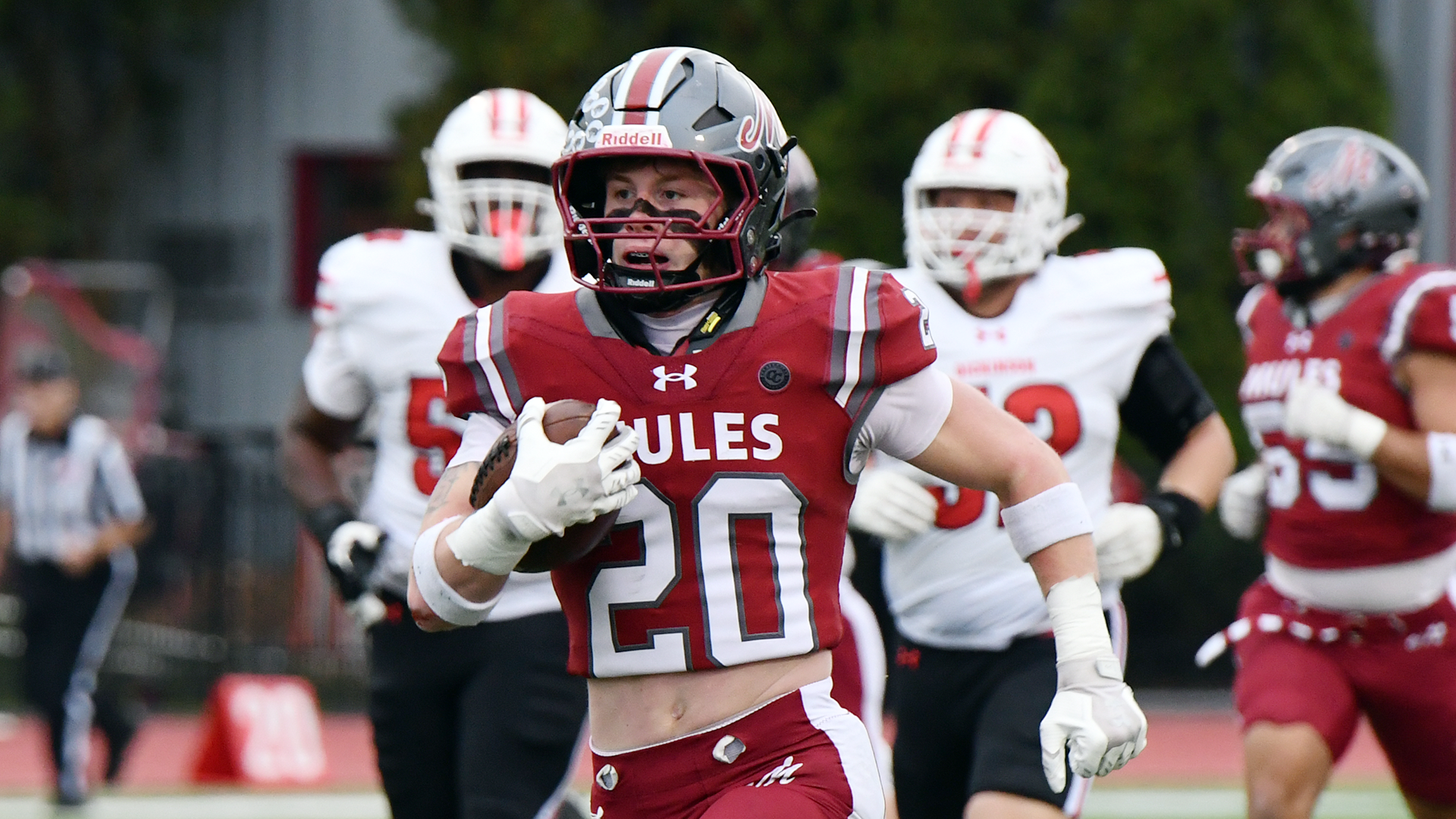 A football player in a red jersey and silver helmet carries the ball in open space