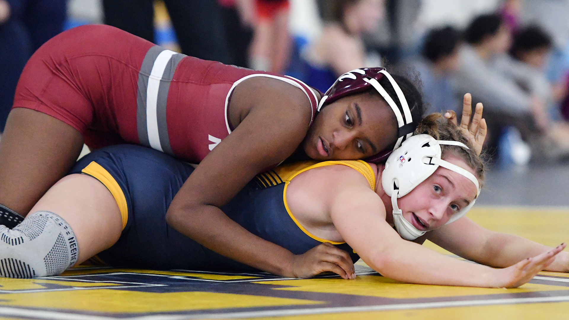 A wrestler in a red singlet rides one in a blue singlet