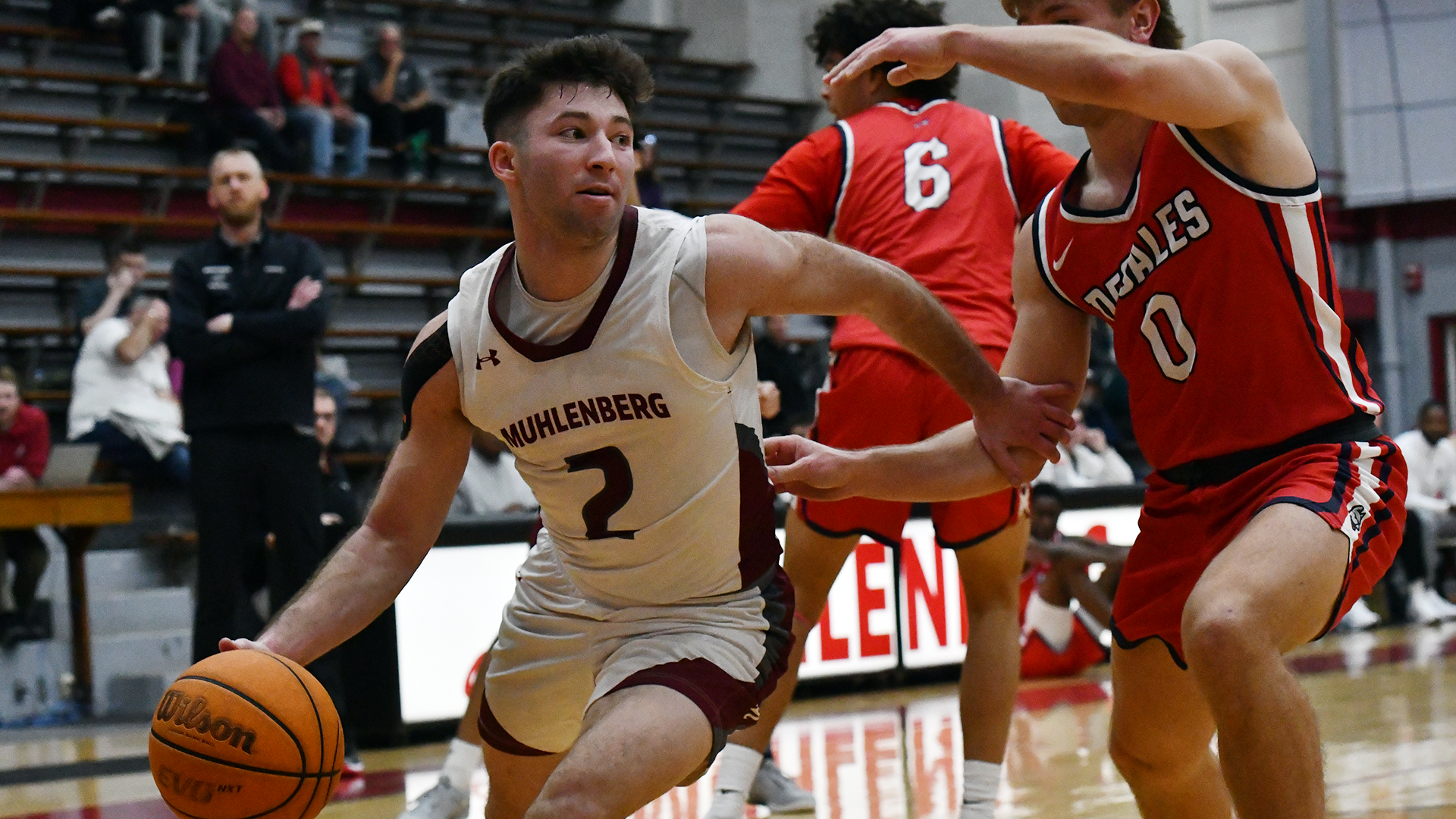 A basketball player in a white jersey drives against a player in a red jersey