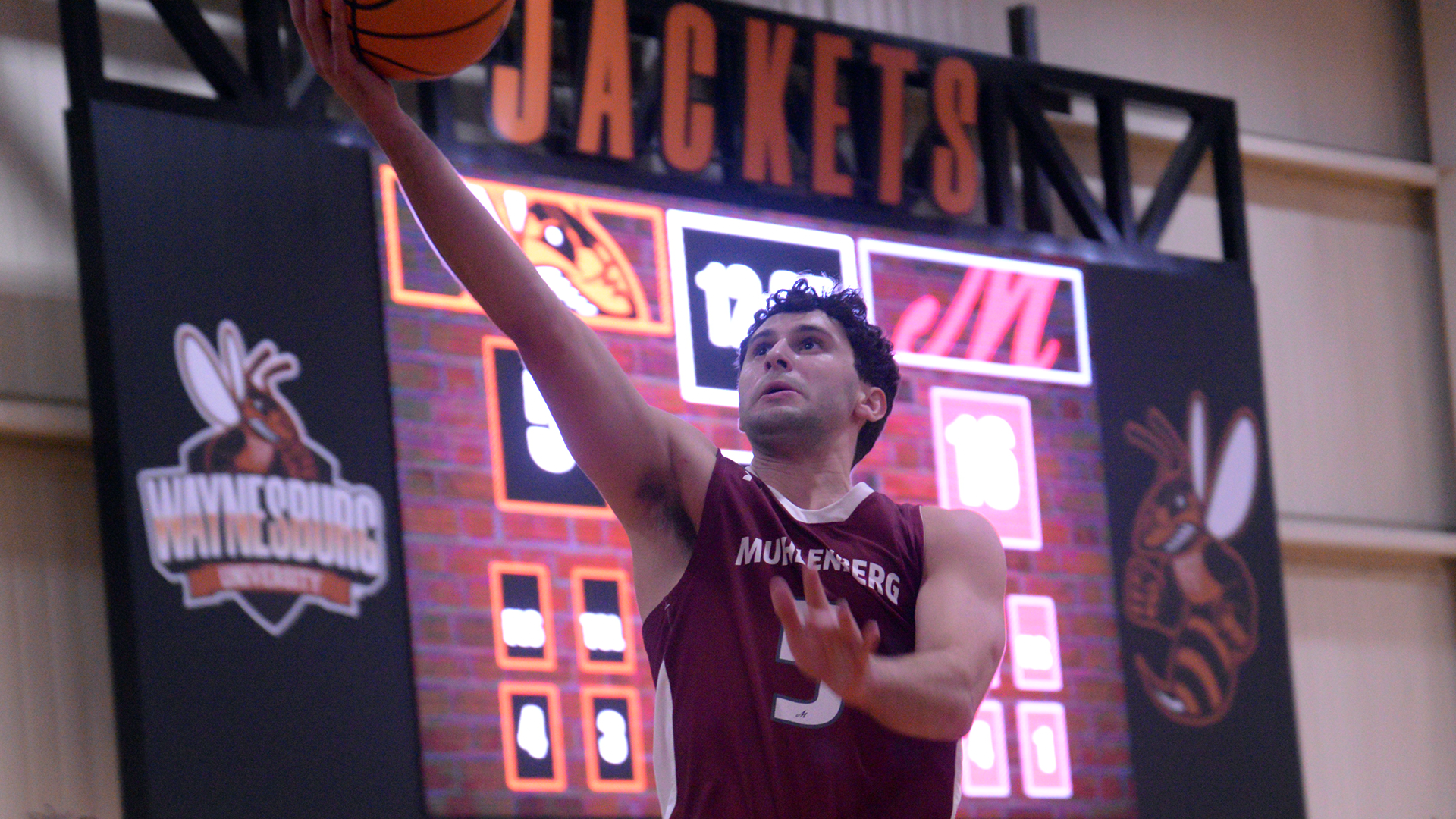A basketball player in a red jersey drives in for a layup