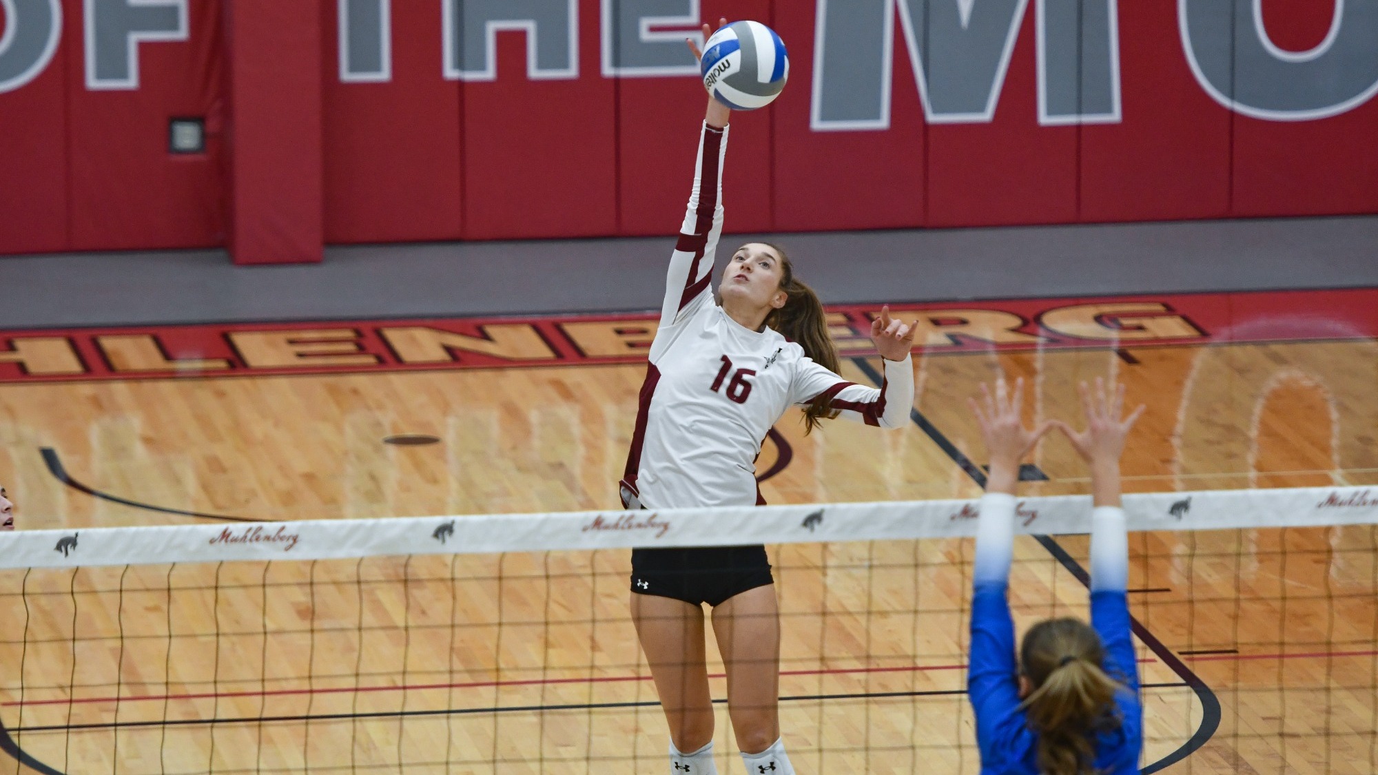 A volleyball player in a white uniform rises at the net to spike the ball