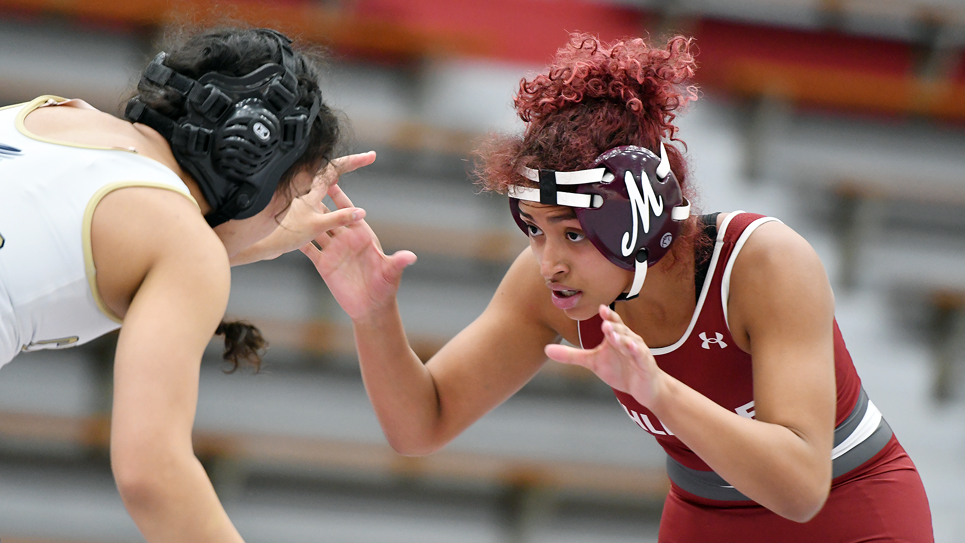 A wrestler in a red singlet and red headgear gets ready to attack her opponent