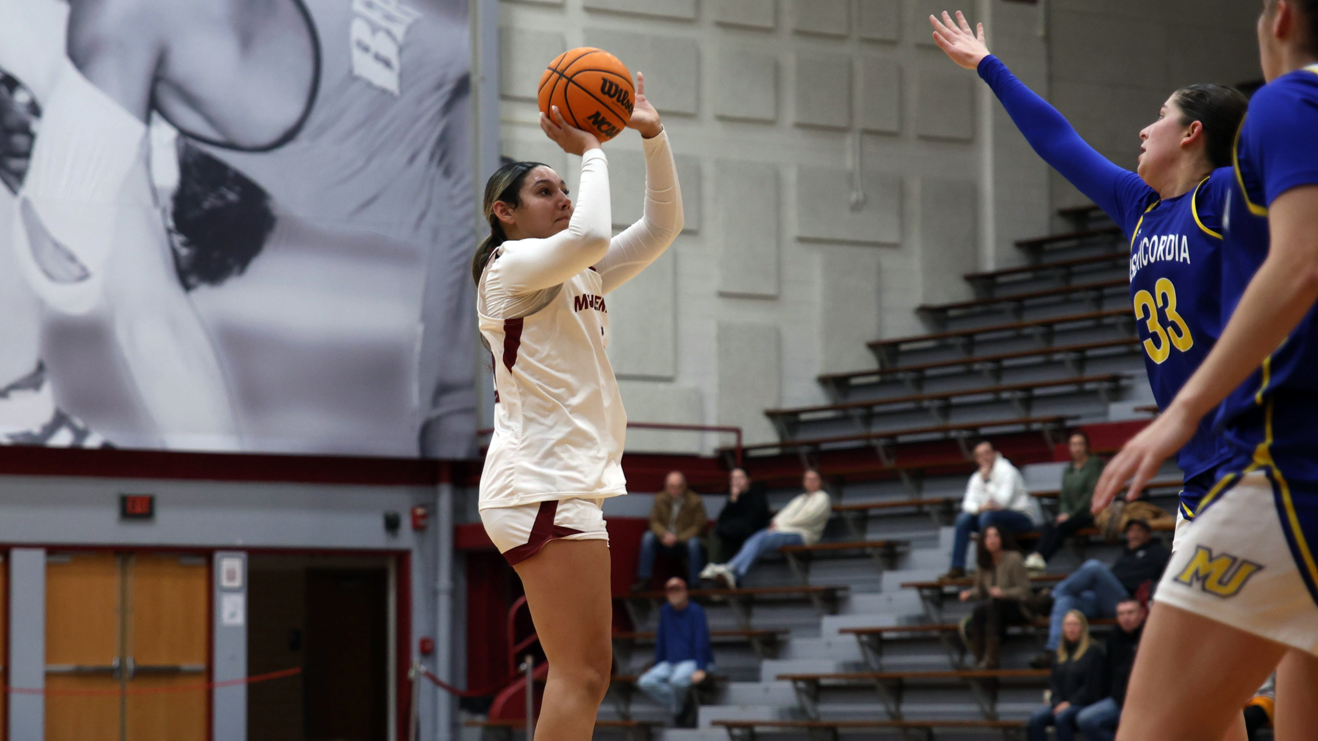 A basketball player in a white uniform shoots as a player in a blue uniform approaches her with an outstretched arm