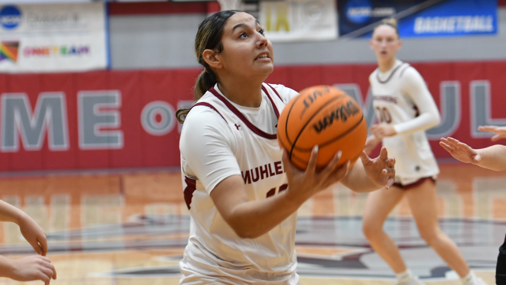 A women's basketball player in white drives to the basket with the ball in her hand