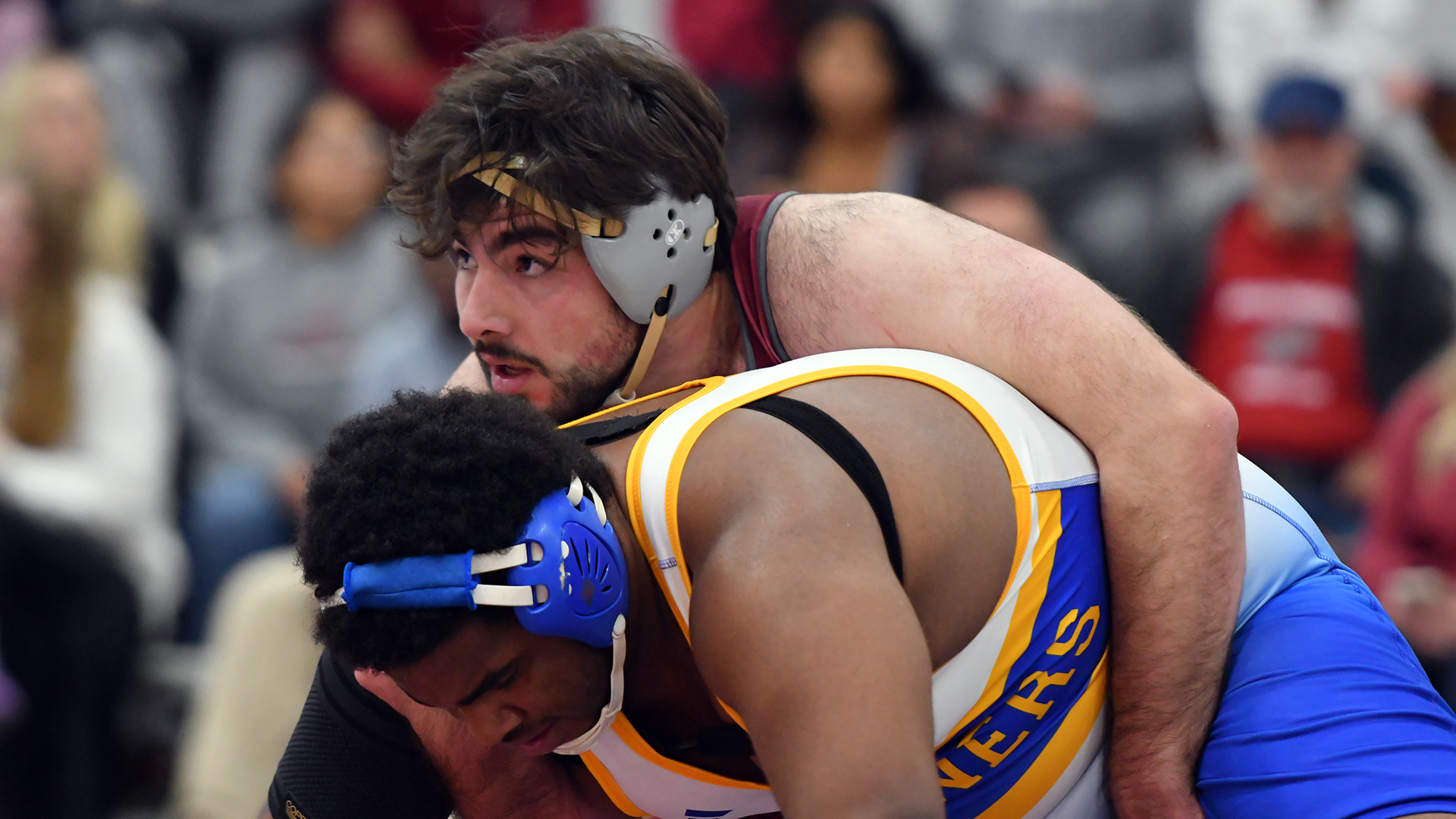 A wrestler in a red singlet rides one in a blue and white singlet