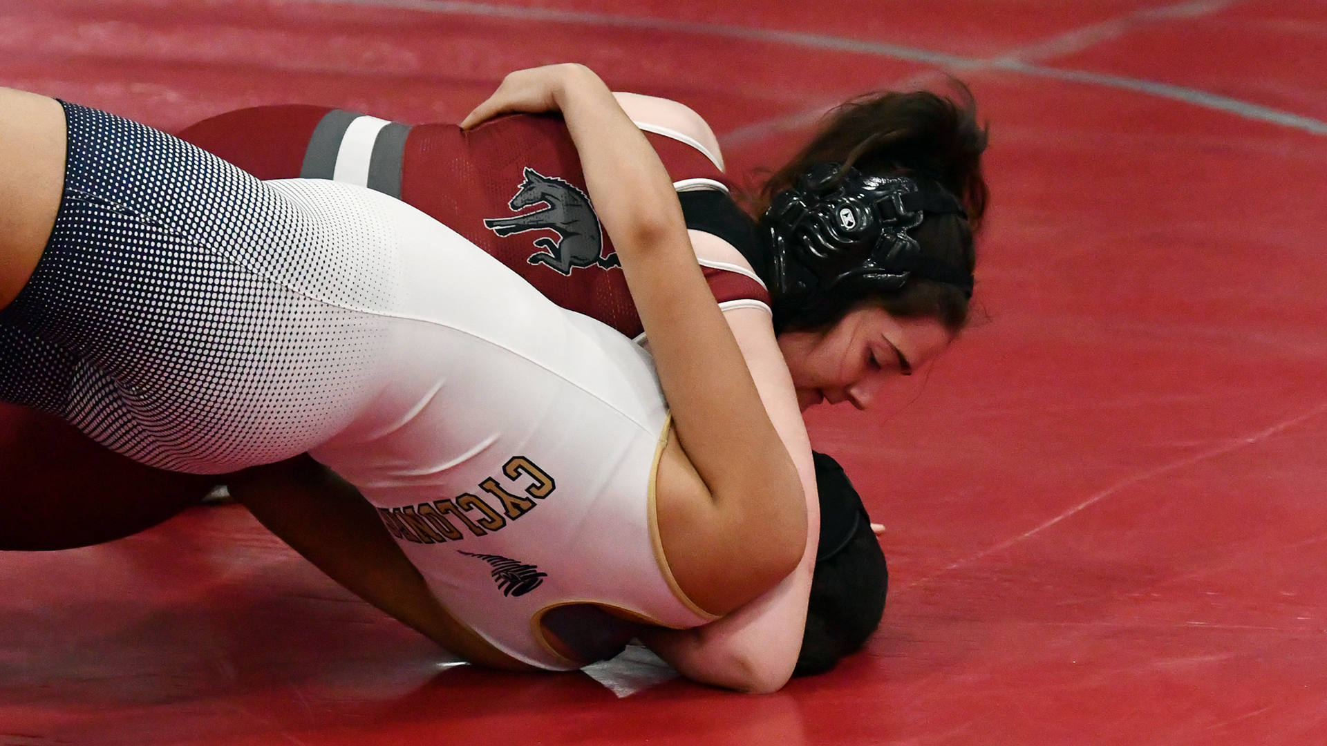 A wrestler in a red singlet with a mule on the back pins one in a white singlet with the word Cyclones on the back
