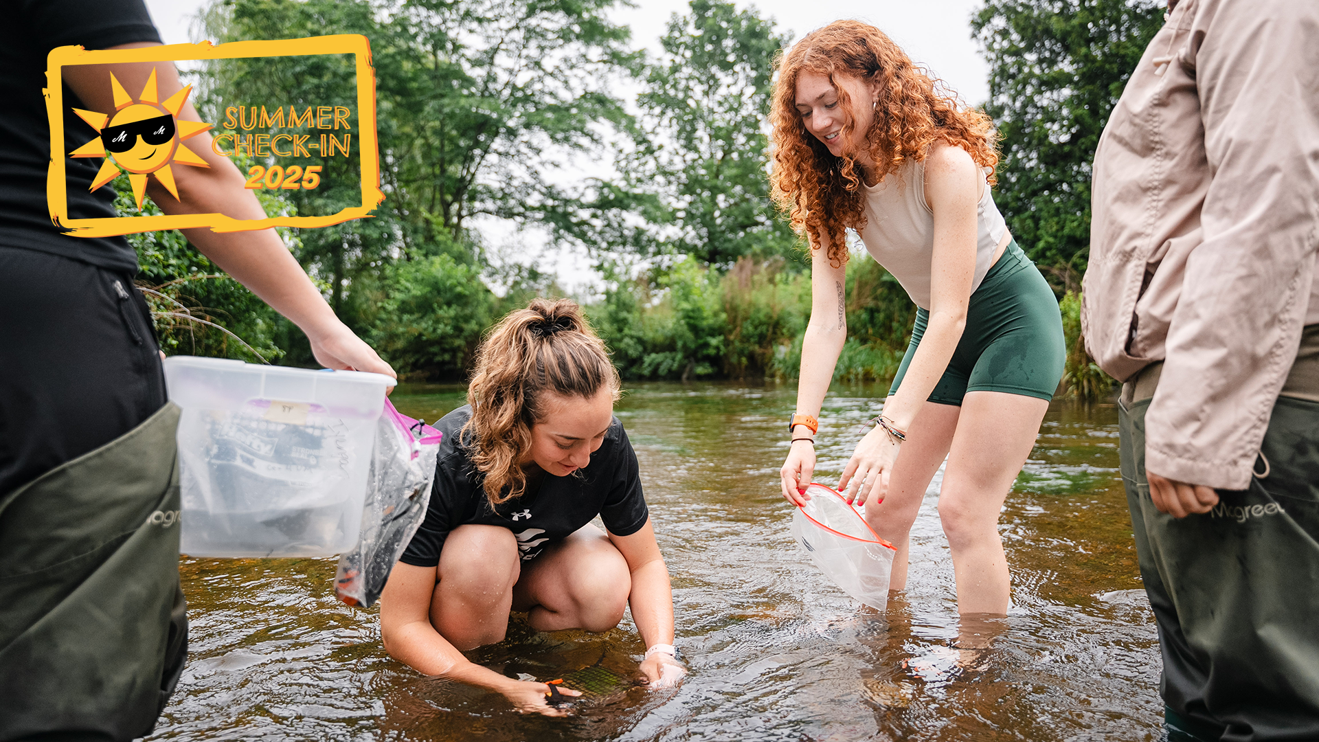 two young women, one kneeling and one standing ankle deep in water, collect samples in a body of water
