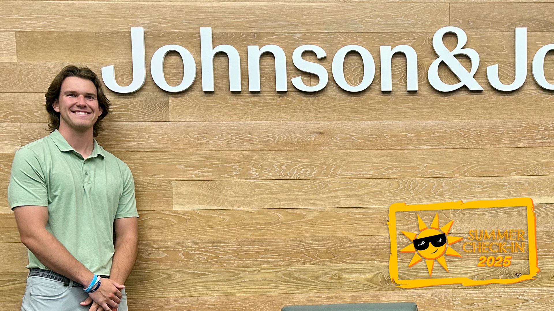 A young man in a light green polo shirt stands in front of a wooden wall with the words Johnson&Johnson