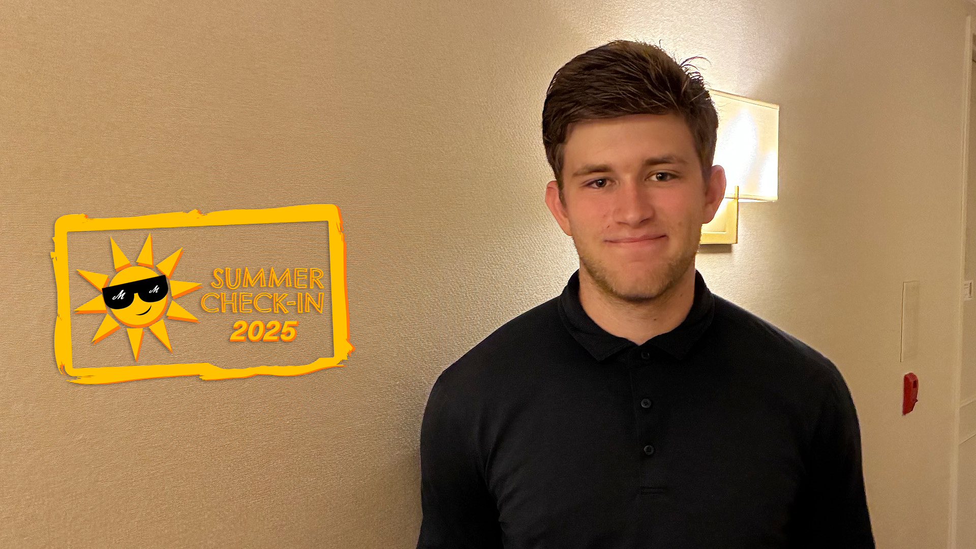 A young man in a black shirt poses in front of a textured white wall