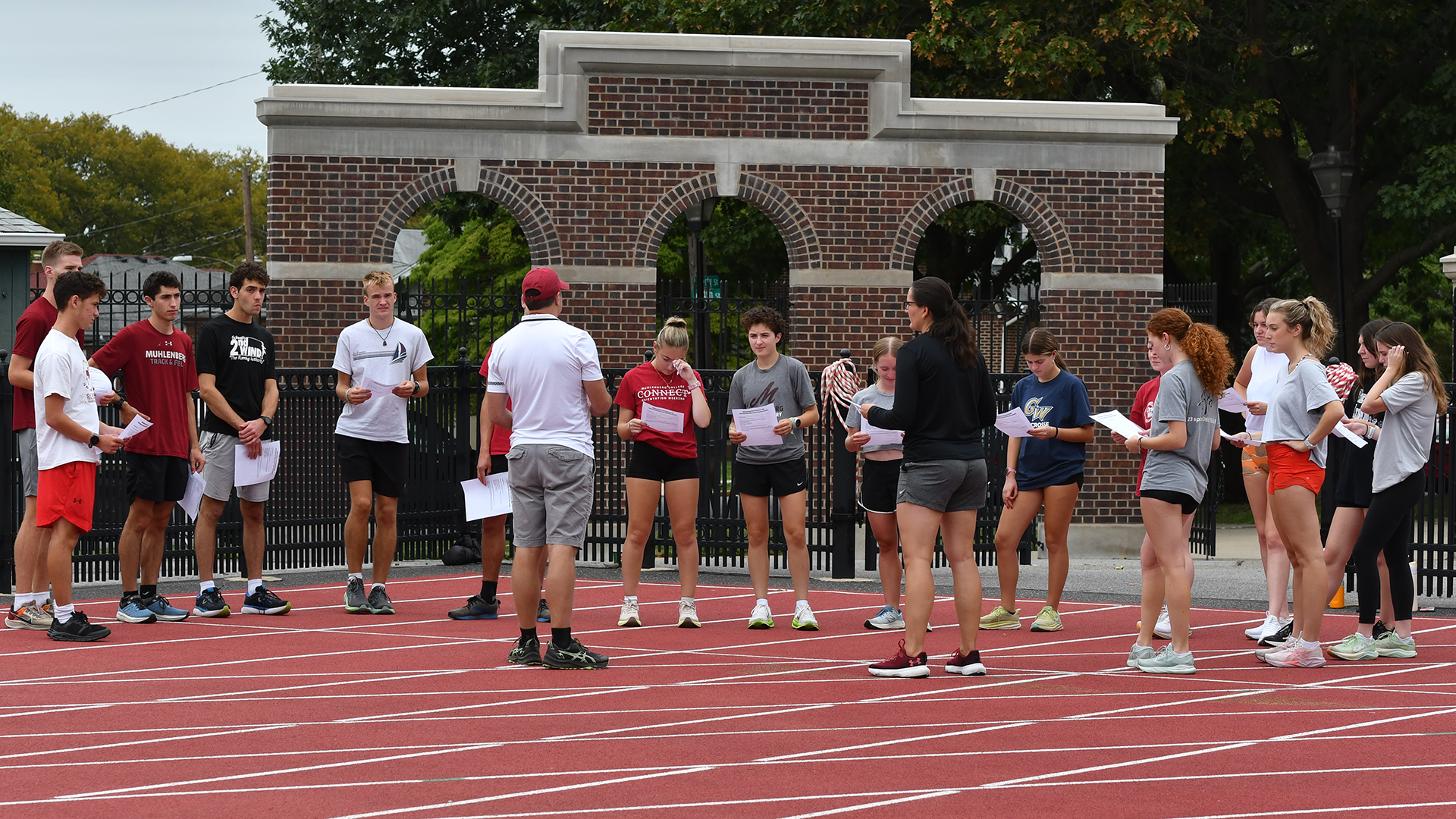 cross country runners stand in a circle outdoors, listening to instructions from a coach
