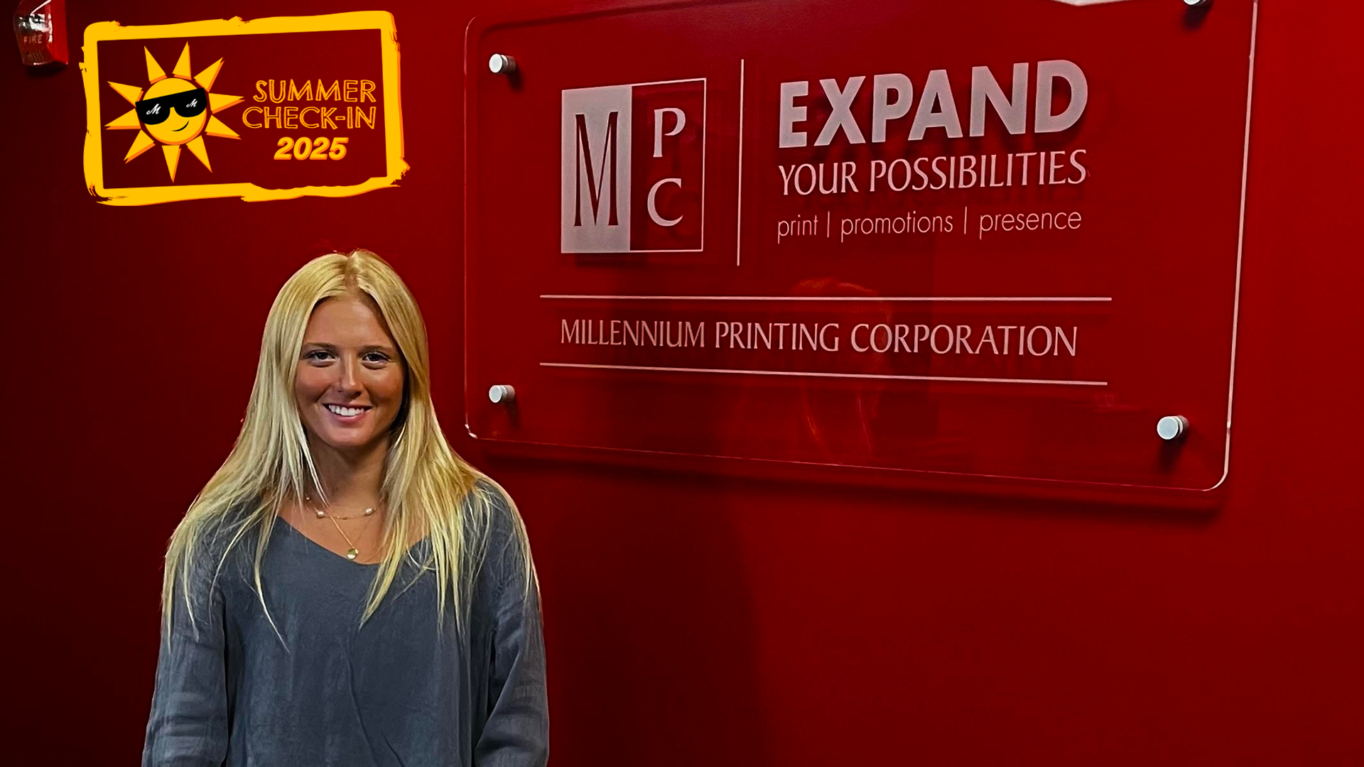 A young woman stands in front of a red wall with the Millenium Printing Corporation logo on it