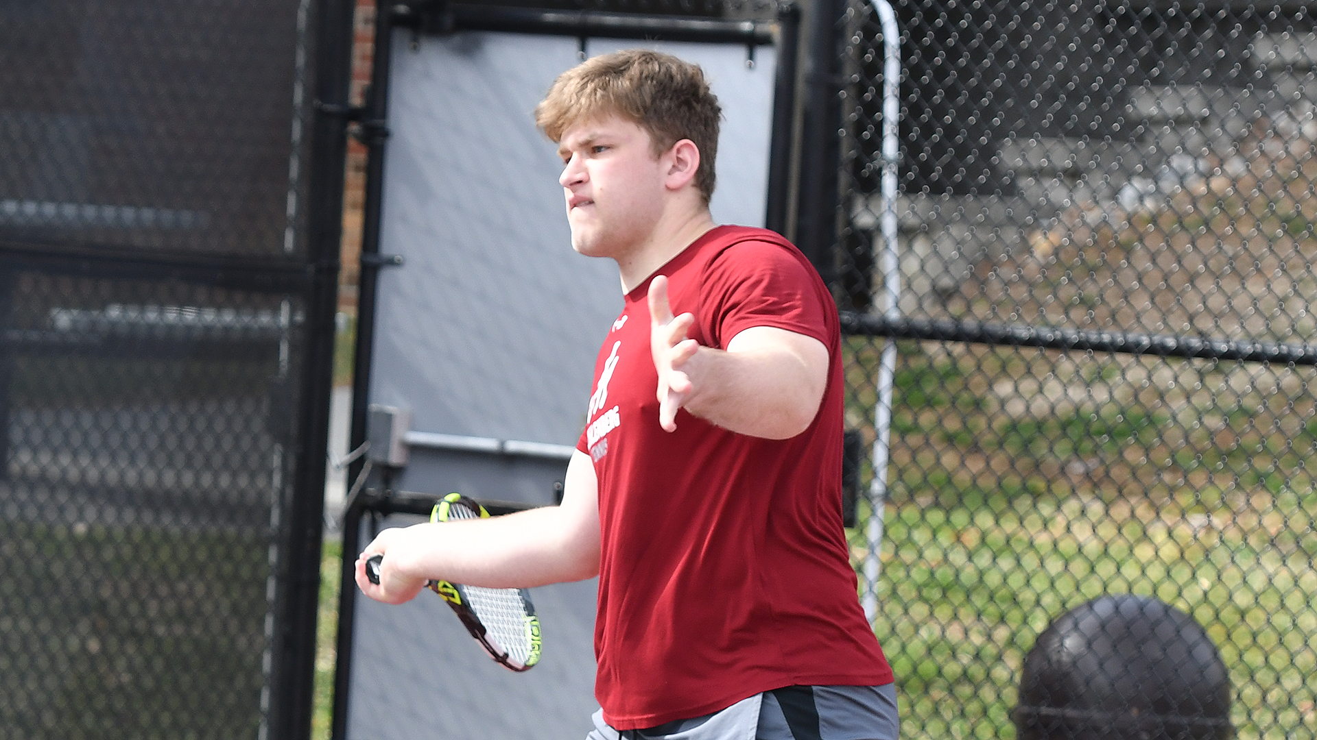 A young man in a red shirt plays tennis