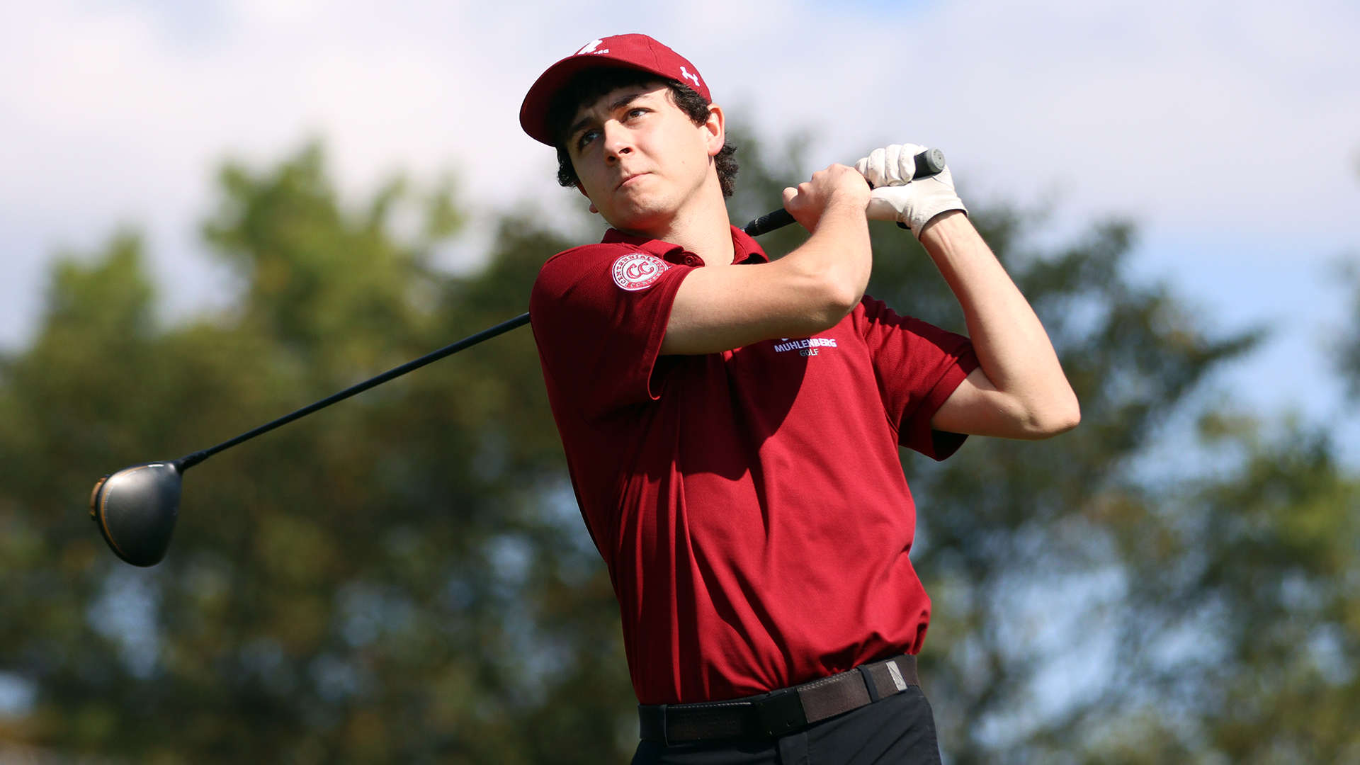 A golfer in a red shirt follows through on his swing