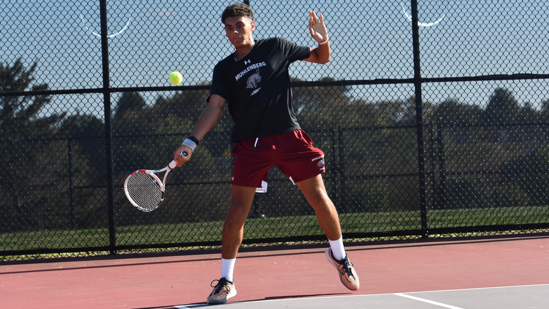 A man in a black shirt hits a tennis forehand on a tennis court