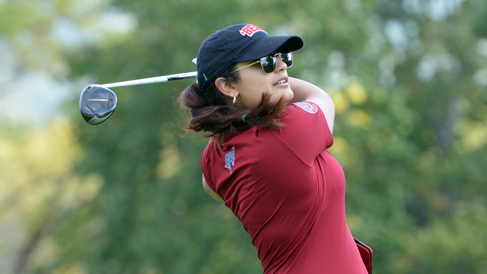 A women's golfer in a red shirt follows through on a swing