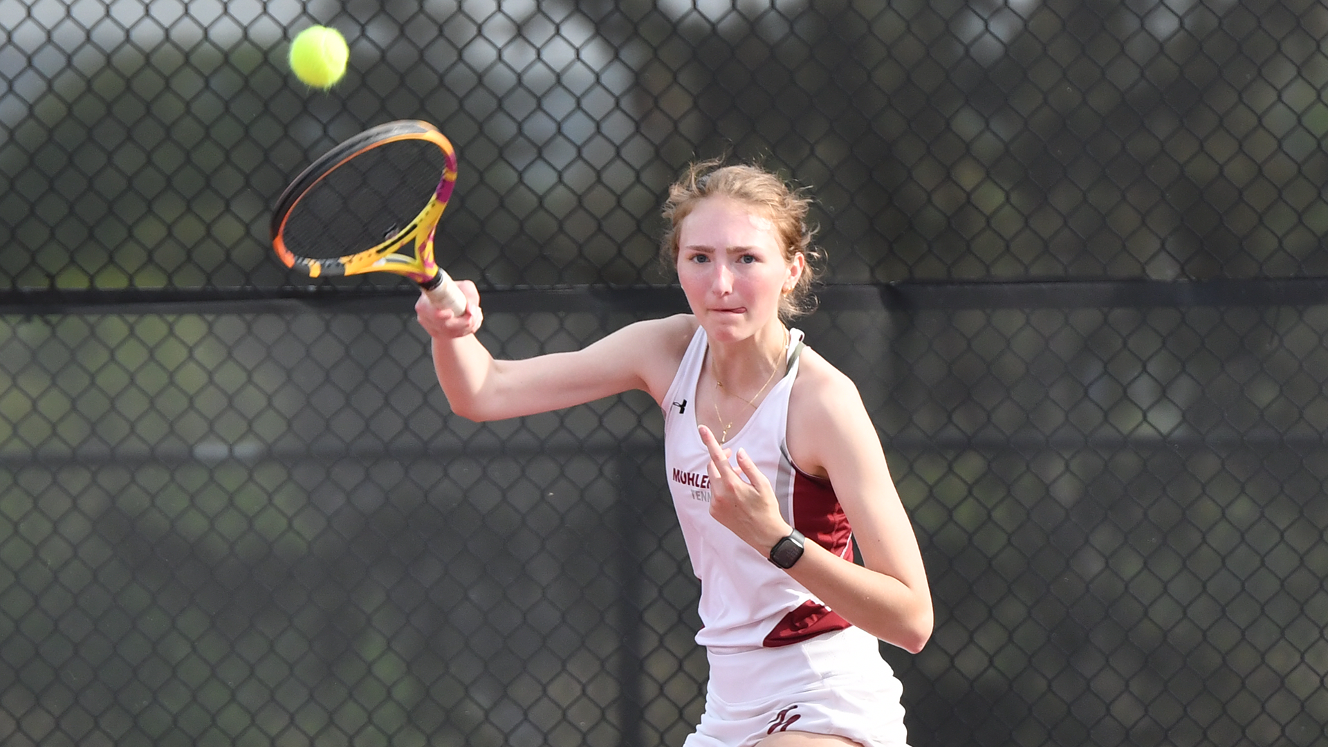 A tennis player in a white uniform follows through after hitting the ball at the net