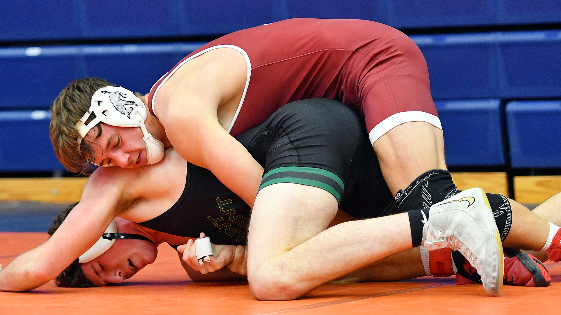 a wrestler in a red singlet rides one in a black singlet