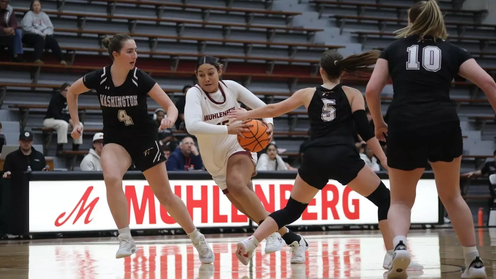 A women's basketball player in a white jersey drives to the basket through a crowd of defenders wearing black jerseys 