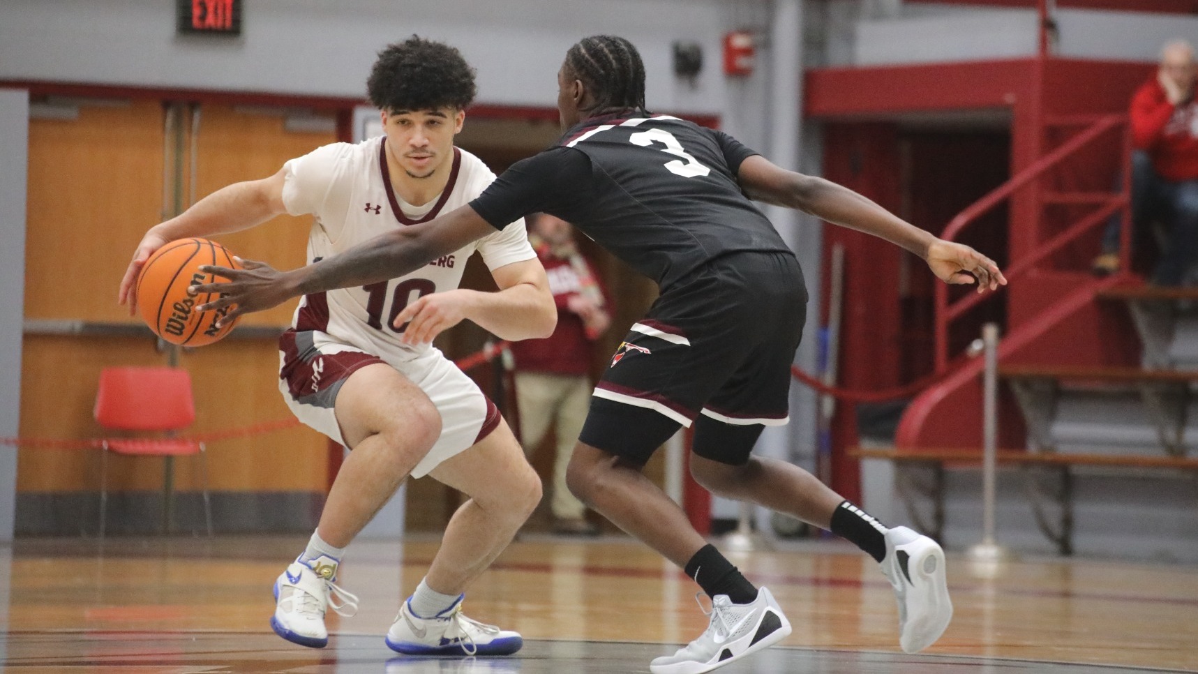 A basketball player in a while uniform dribbles while being guarded by a player in a black uniform