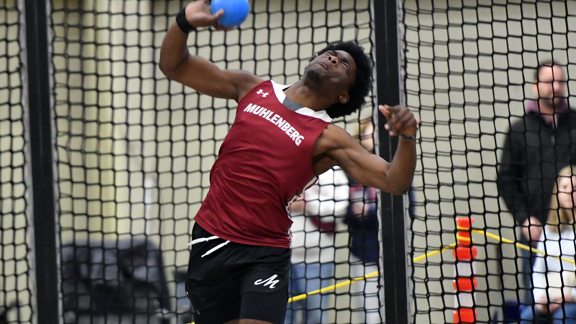 a shot putter in a red uniform releases a blue shot