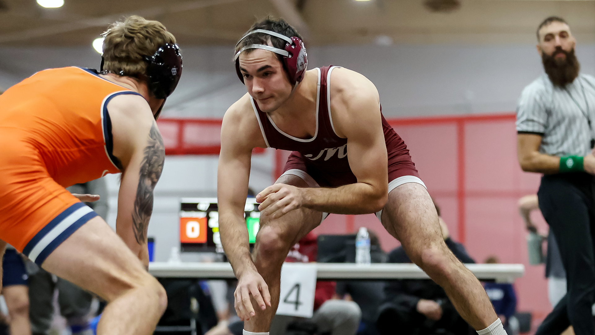 a wrestler in a red singlet in his stance, sizing up his opponent