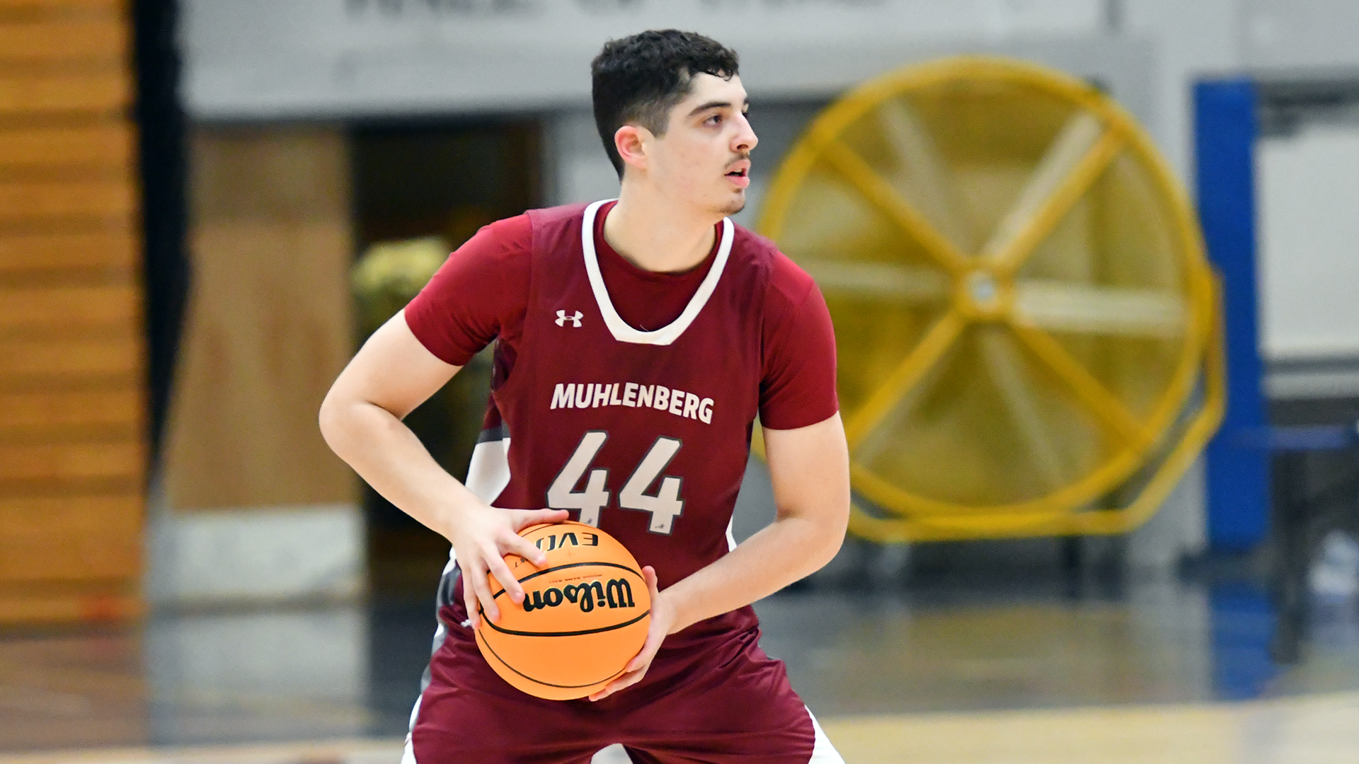 a basketball player in a red uniform holds the ball on his right while looking to his left
