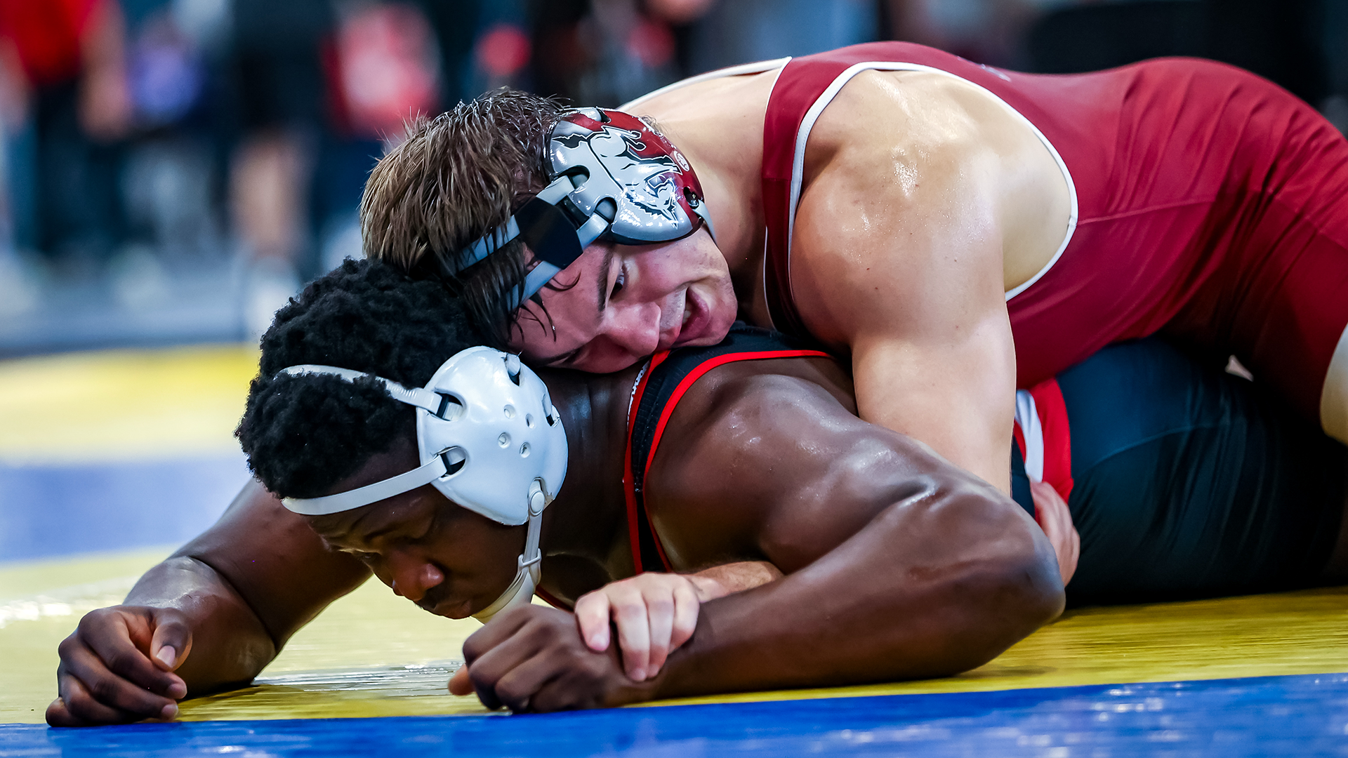 a wrestler in a red singlet rides one in a blue singlet