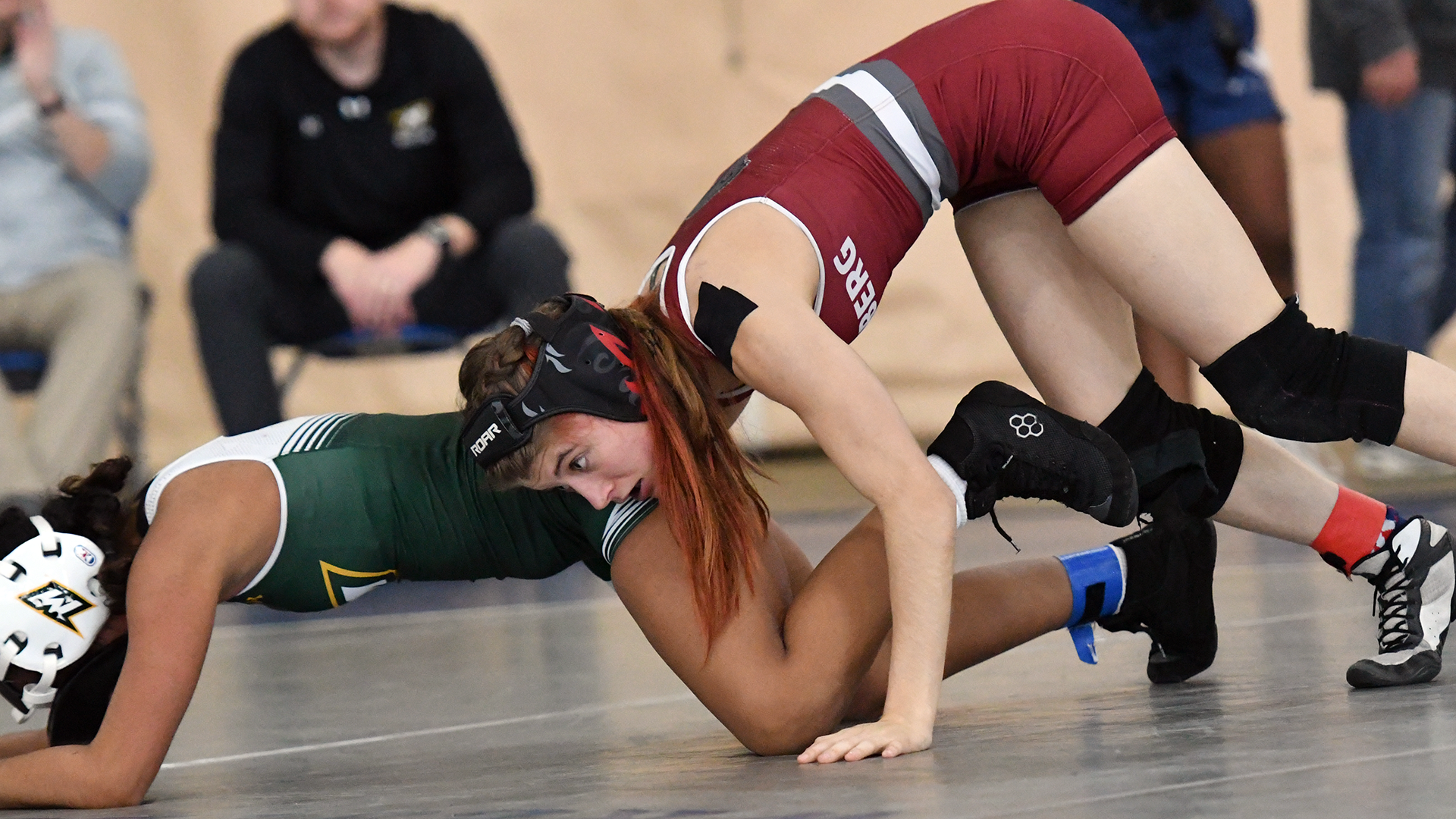 a wrestler in a red singlet takes down a wrestler in a green singlet