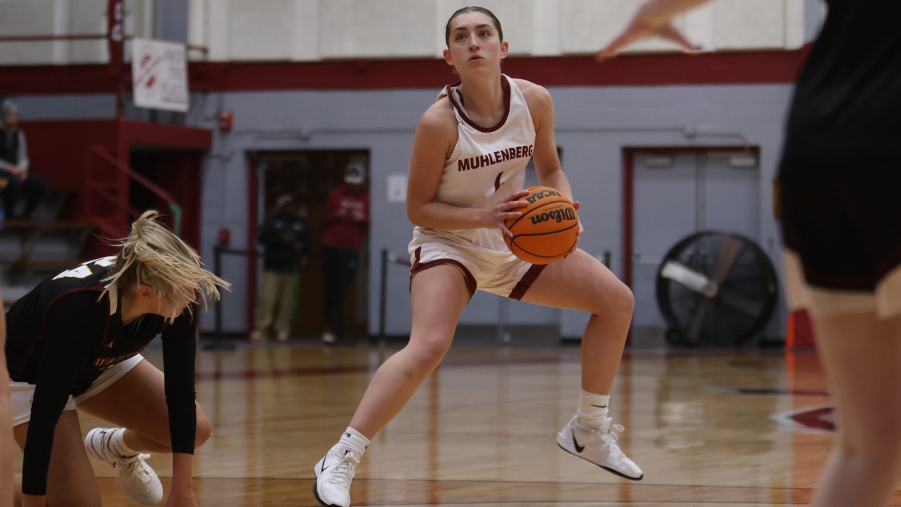 A player in a white uniform attempts a step-back jumpshot over a black uniformed player on the ground