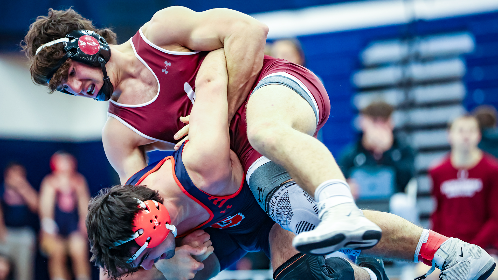 a wrestler in a red singlet works the arm of a wrestler in a blue singlet