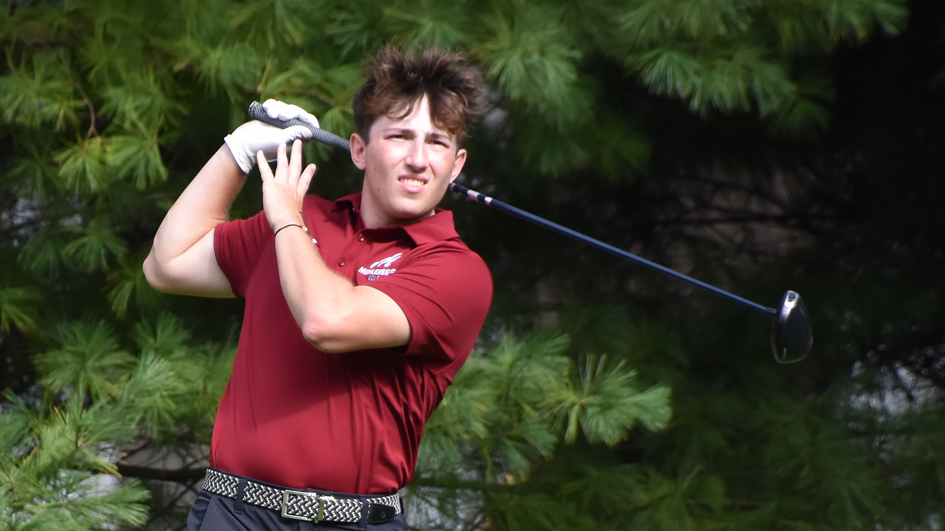 a golfer in a red shirt following the path of the ball after hitting a drive