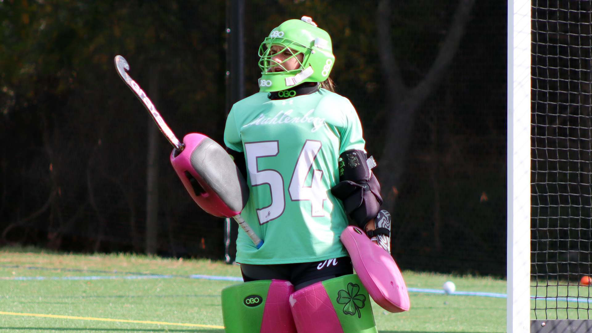 a field hockey goalie in a green top standing in front of the cage with her stick in the air