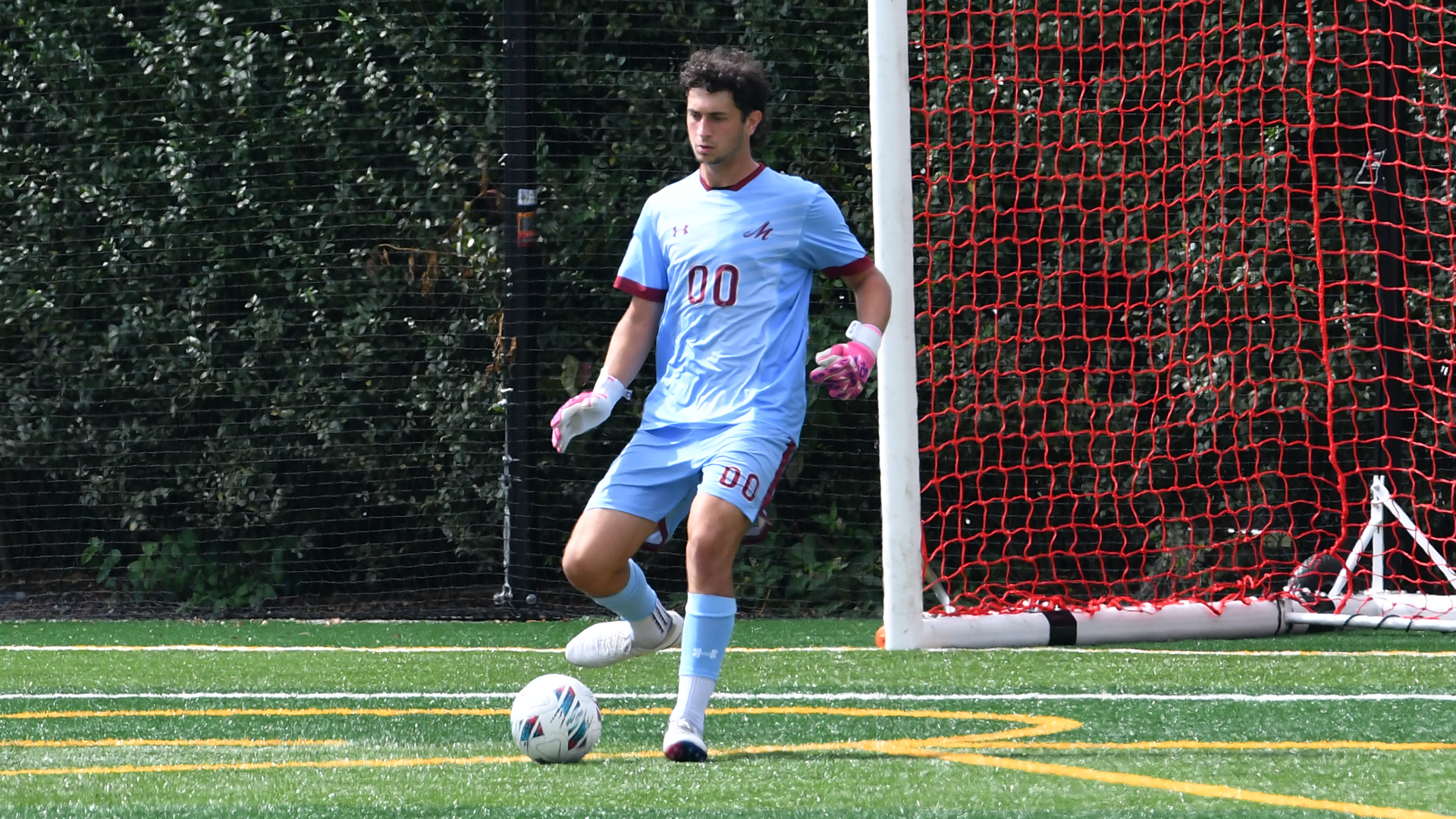 a goalie in a light blue uniform kicking the ball on a green field