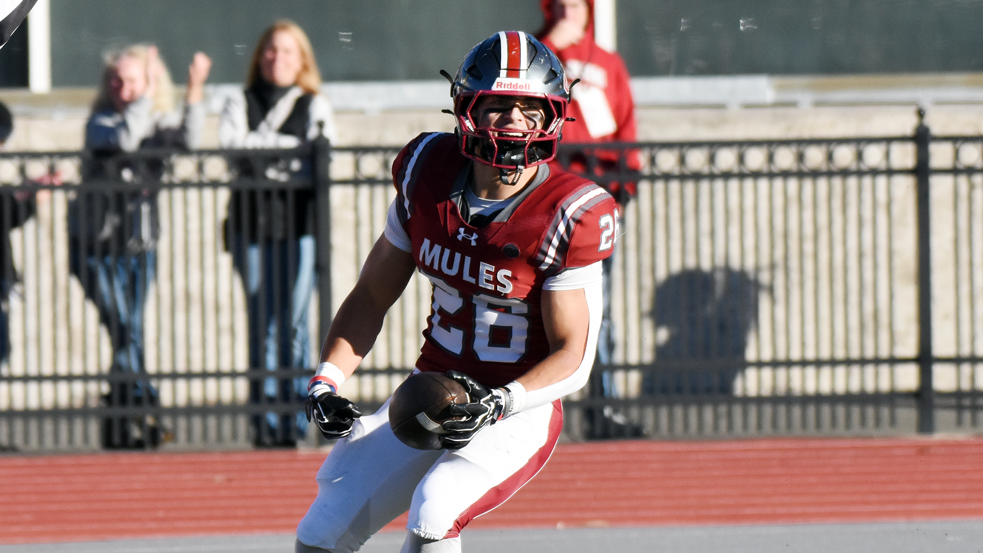 a football player in a red jersey, white pants, and a silver helmet celebrating in the end zone after catching a ball on a sunny day
