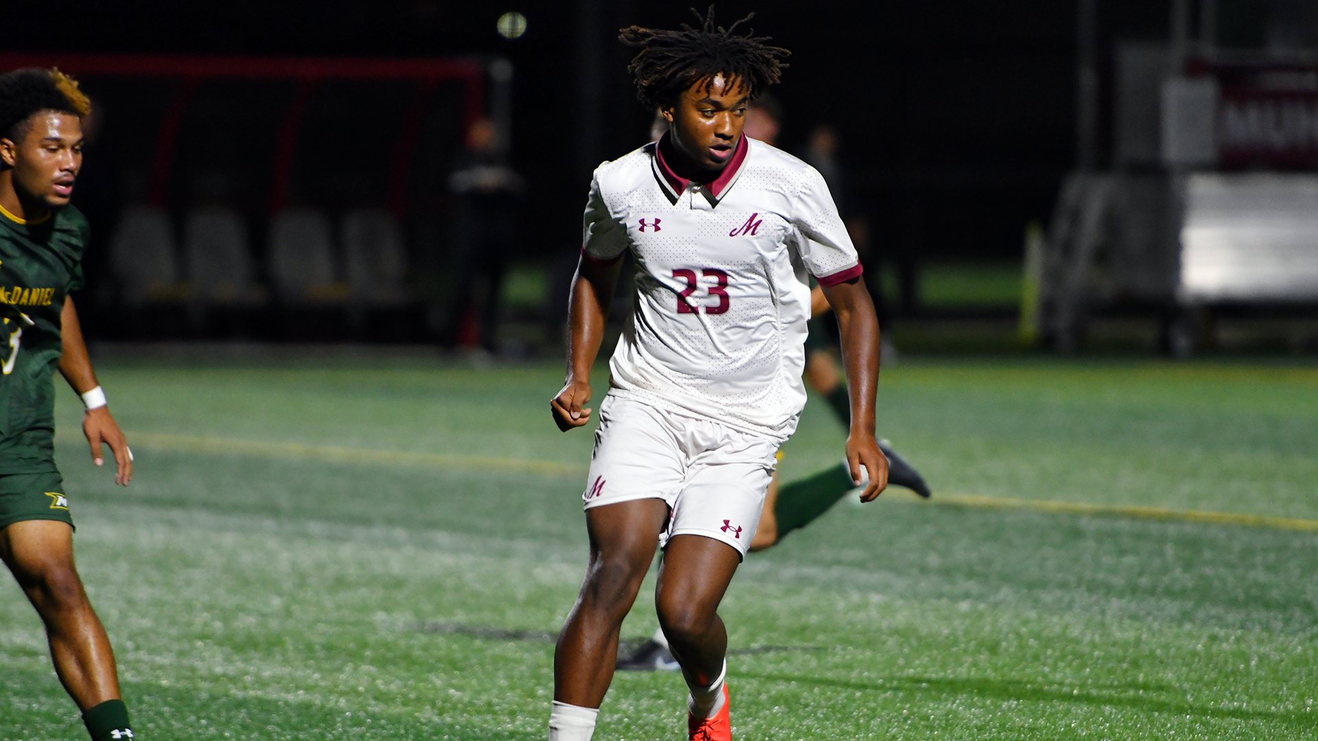 a men's soccer player in a white uniform dribbling during a night game