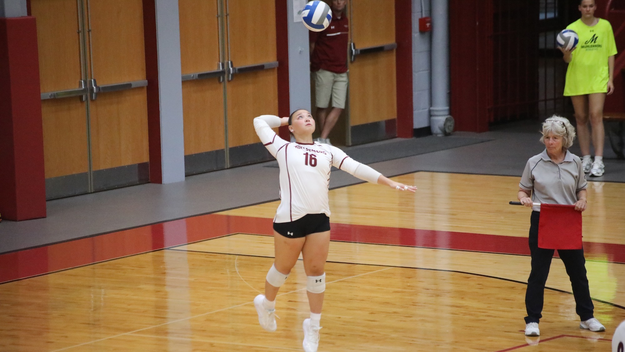 A volleyball player in a white uniform rises to swat a serve in a gym 