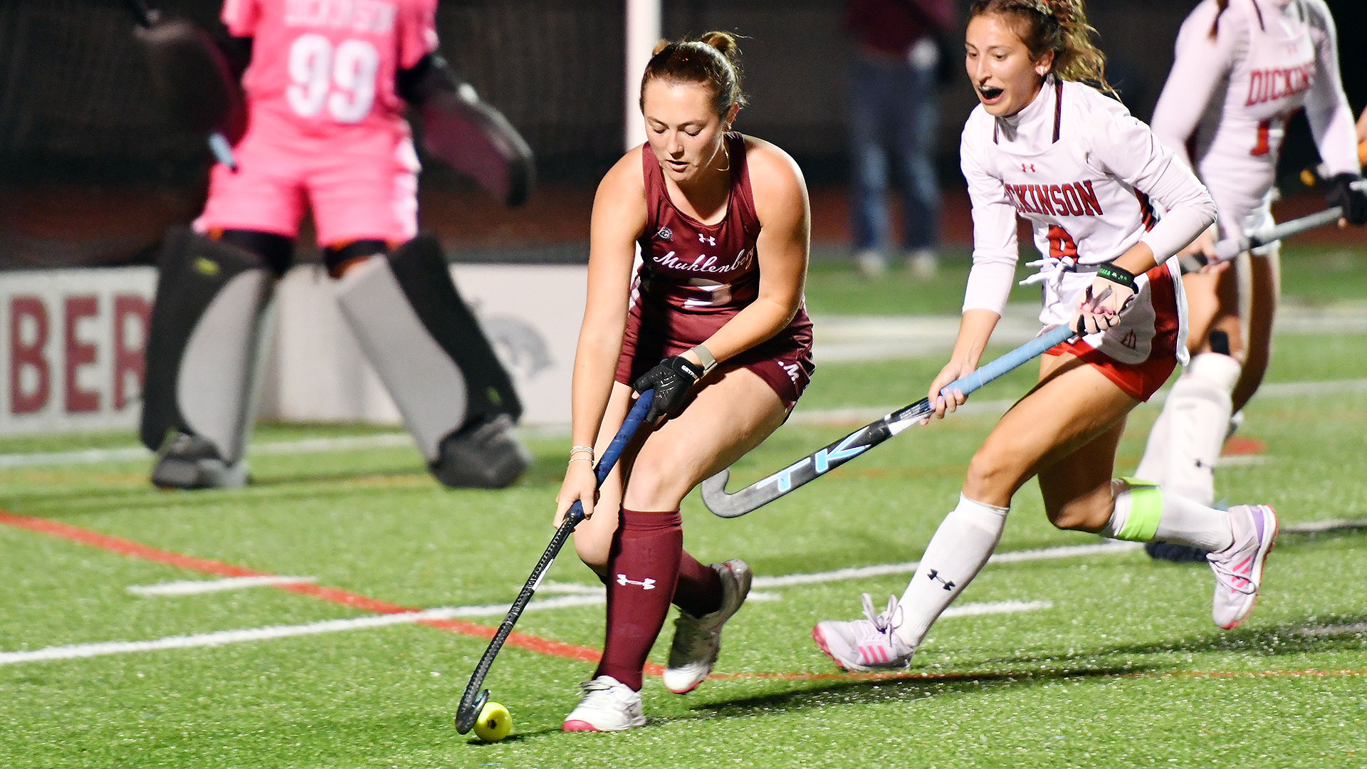 a field hockey player in a red uniform dribbling at night while being guarded by a player in a white uniform
