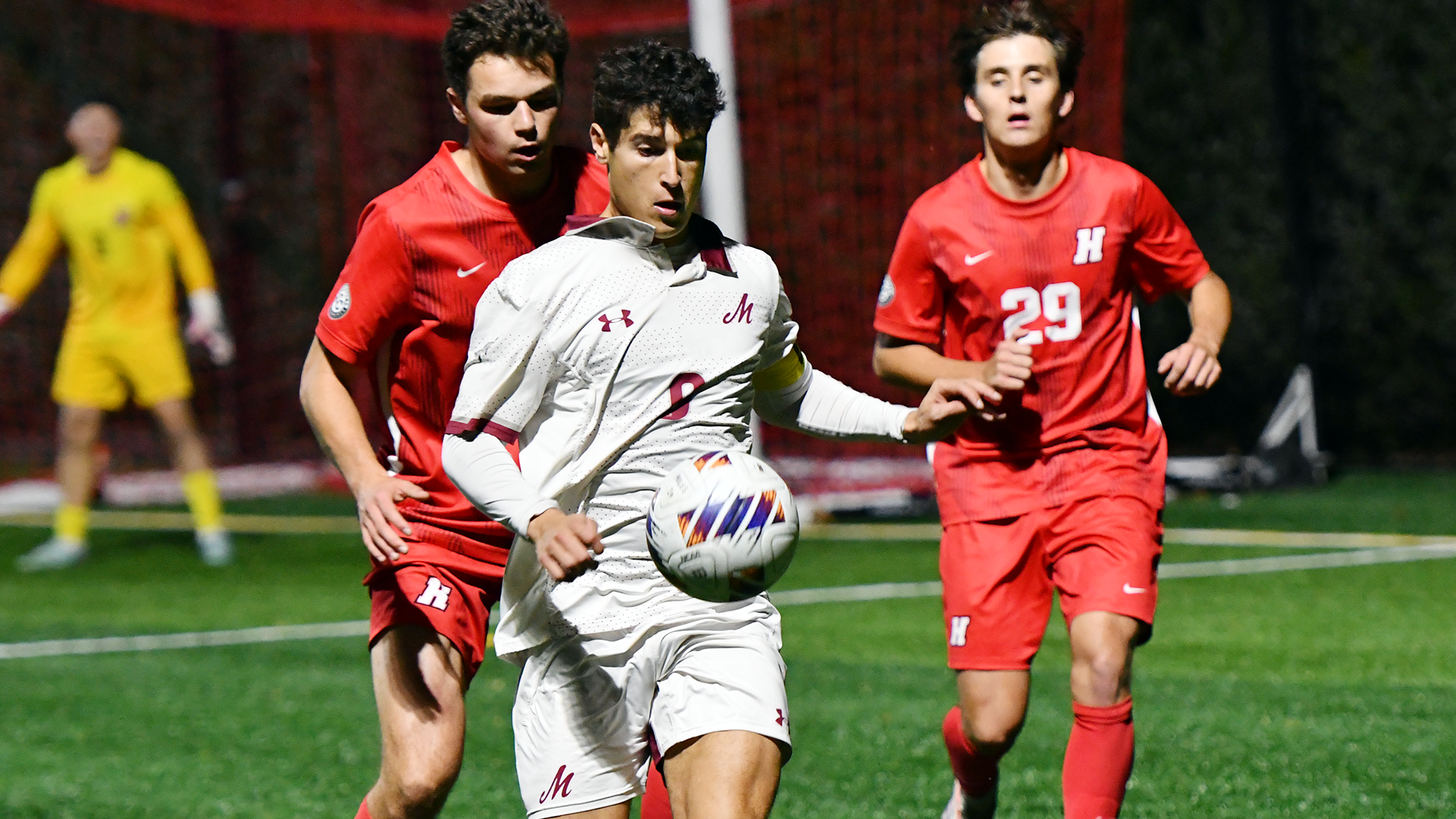a soccer player in a white uniform dribbling the ball with two players in red uniforms behind him