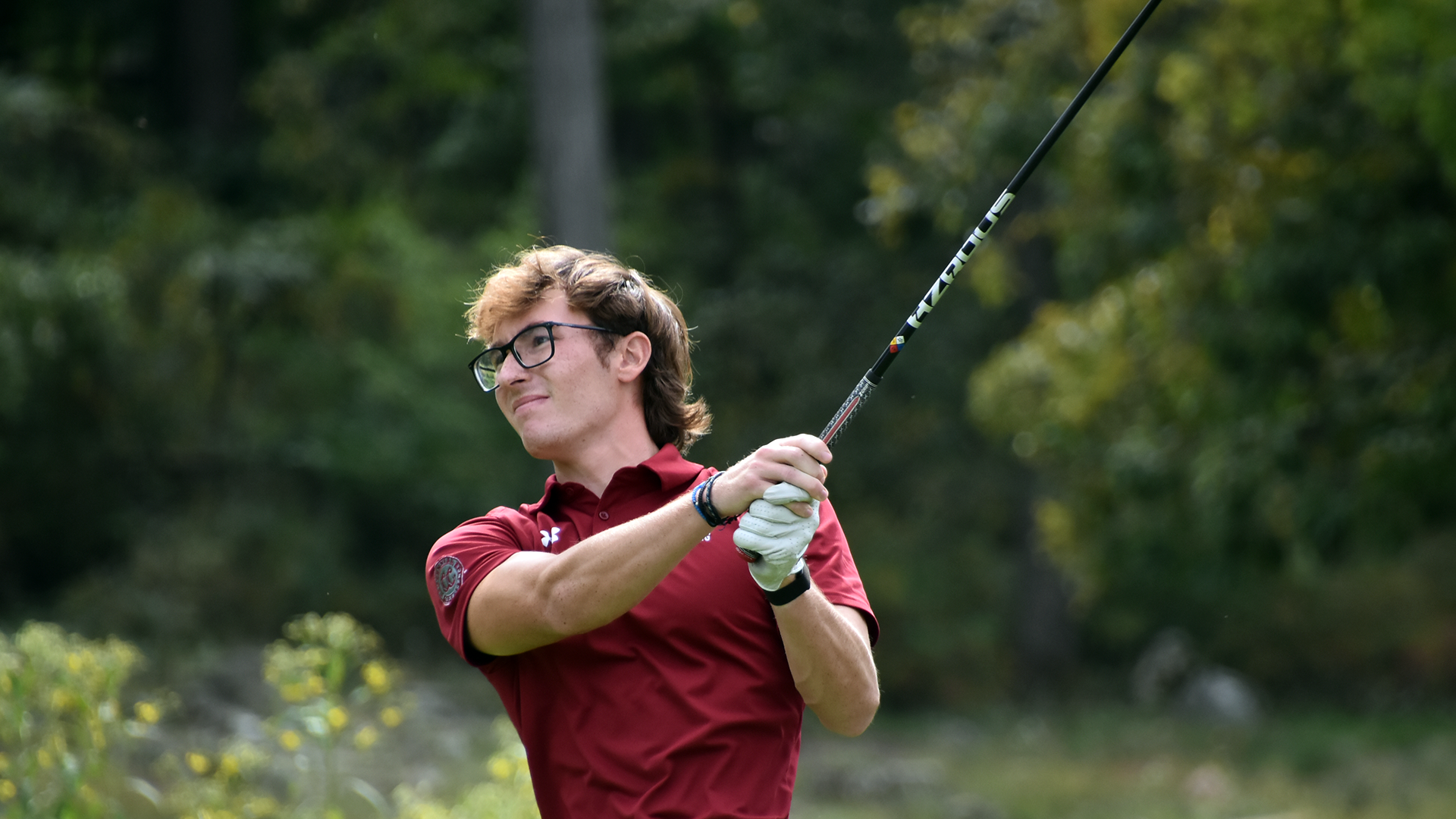 a golfer in a red polo top follows through on a swing