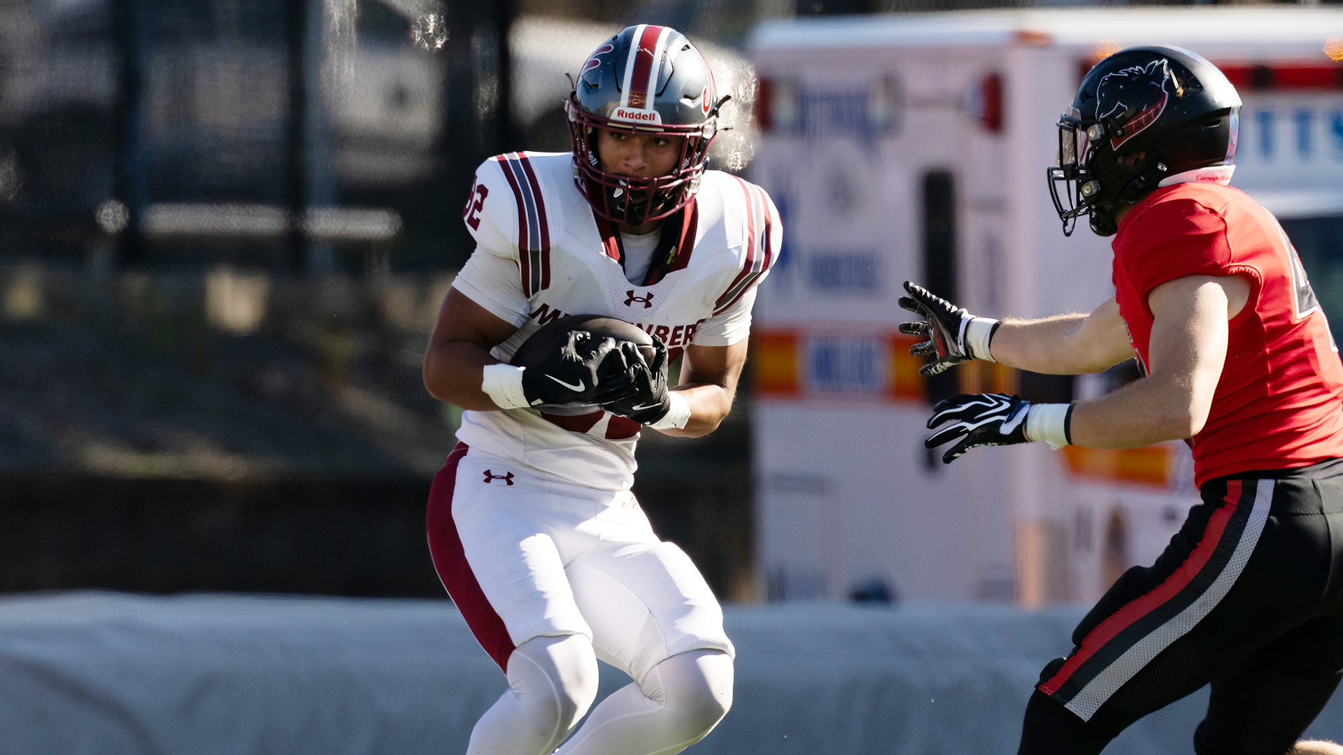 a football player in a white jersey and silver helmet catching a pass while being defended by a player in a red jersey and black helmet
