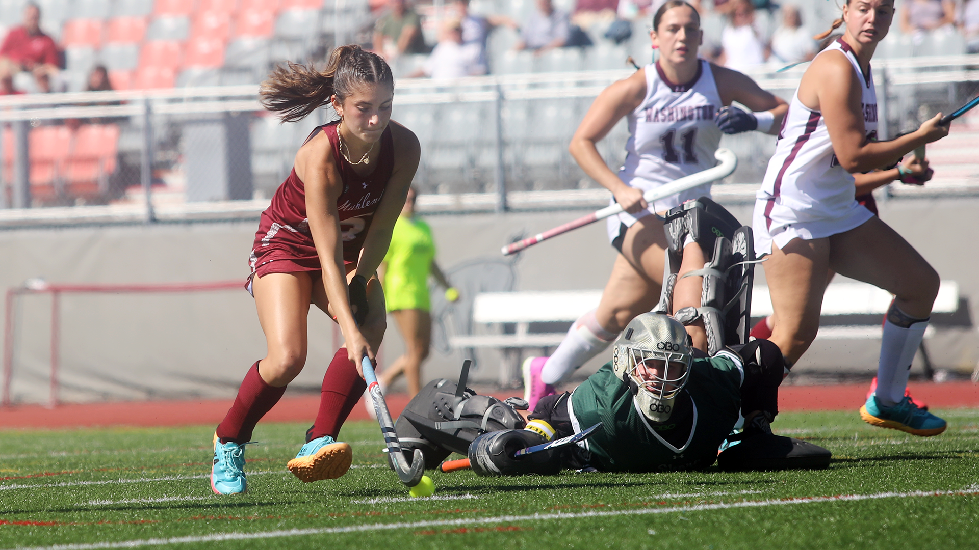 a field hockey player in a red jersey preparing to shoot the ball with the goalie on the ground behind her