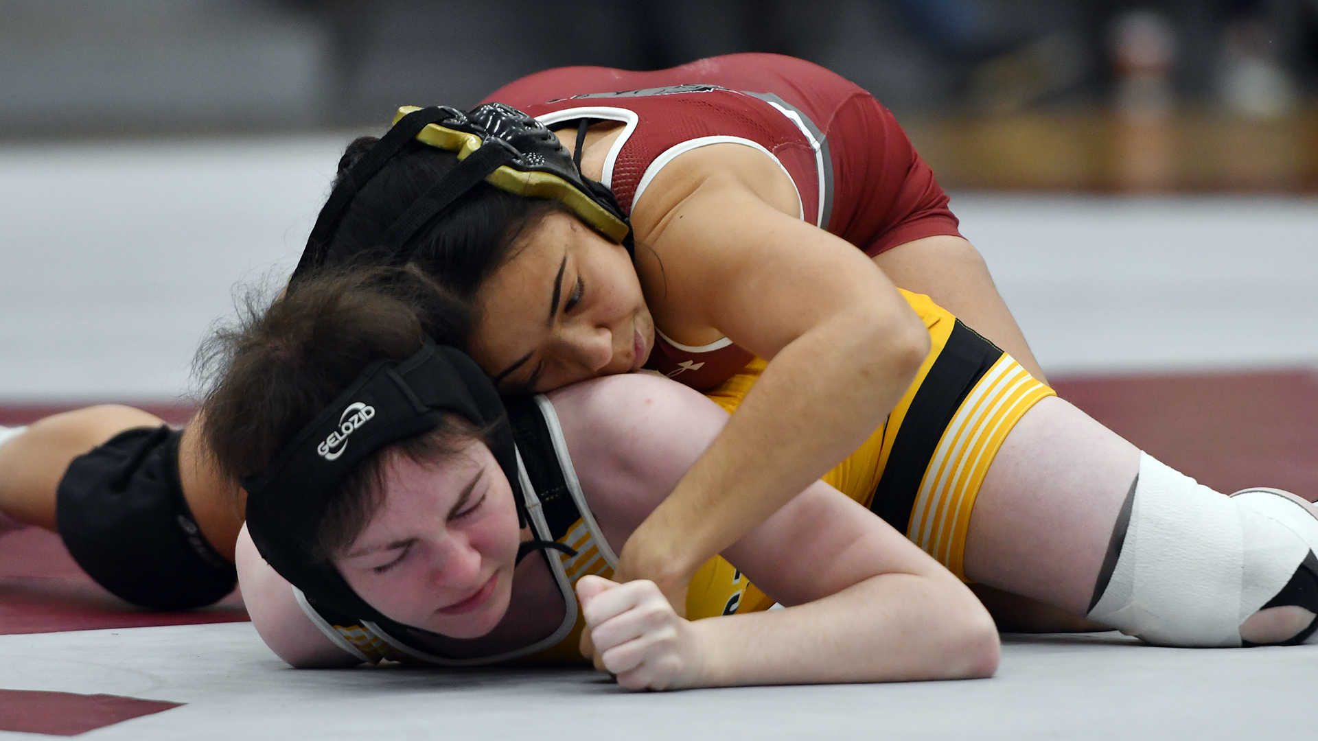 a wrestler in a red singlet on top of one in a yellow singlet