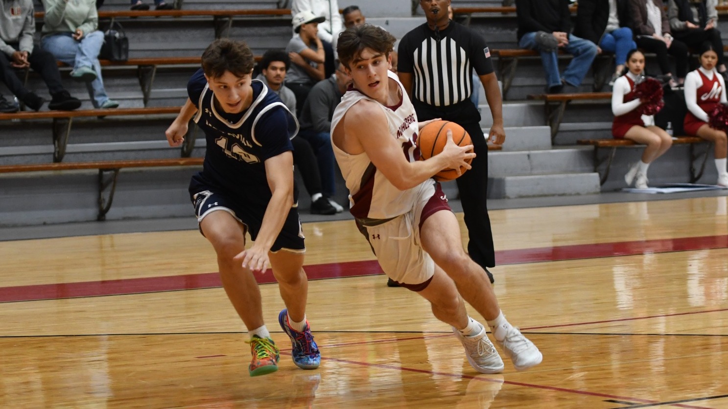 A Muhlenberg men’s basketball player in white drives to the basket while being closely guarded by a defender in blue