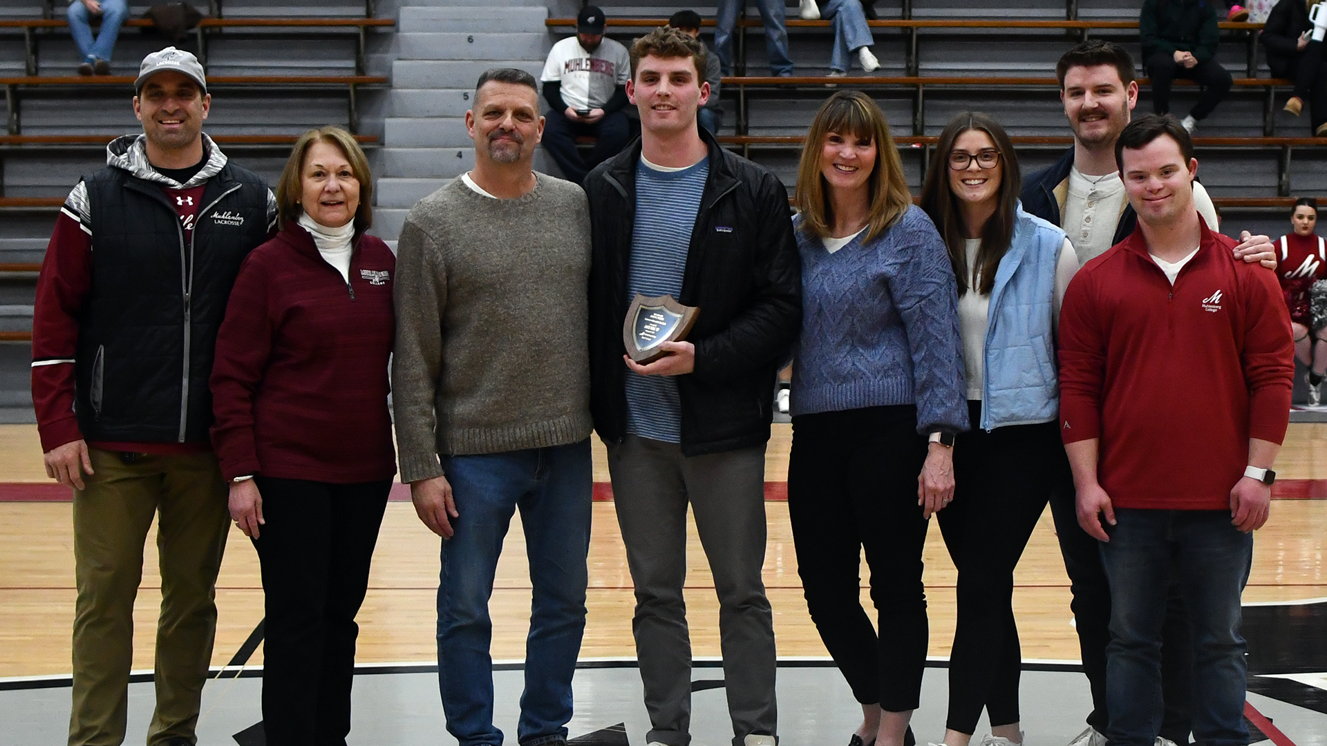 eight people in a row posing for a picture in the gym; the young man fourth from left is holding a plaque