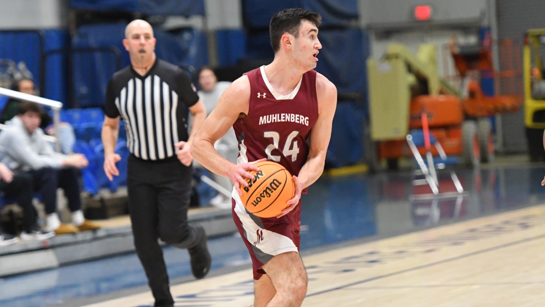A Muhlenberg men’s basketball player in a maroon jersey dribbles up the court