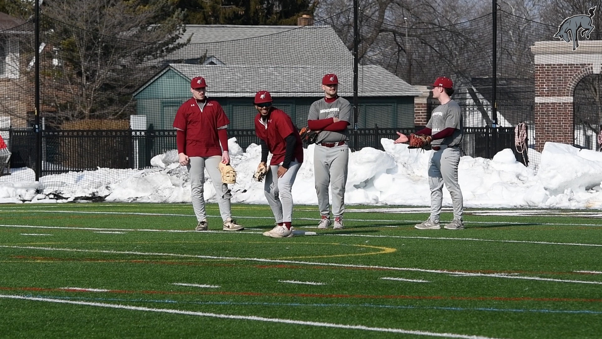 four baseball players holding gloves stand outside on a turf field