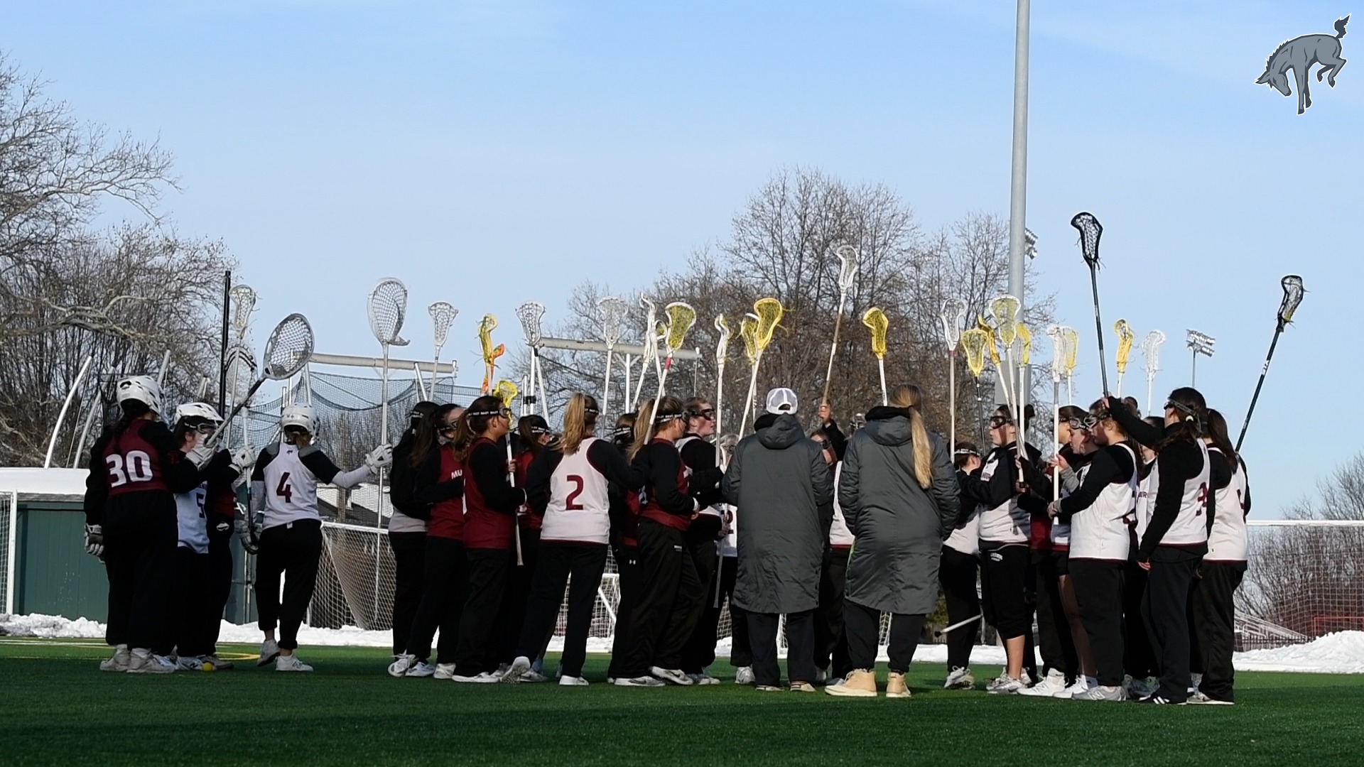 women's lacrosse players dressed in warm clothing put their sticks up in a team huddle outdoors
