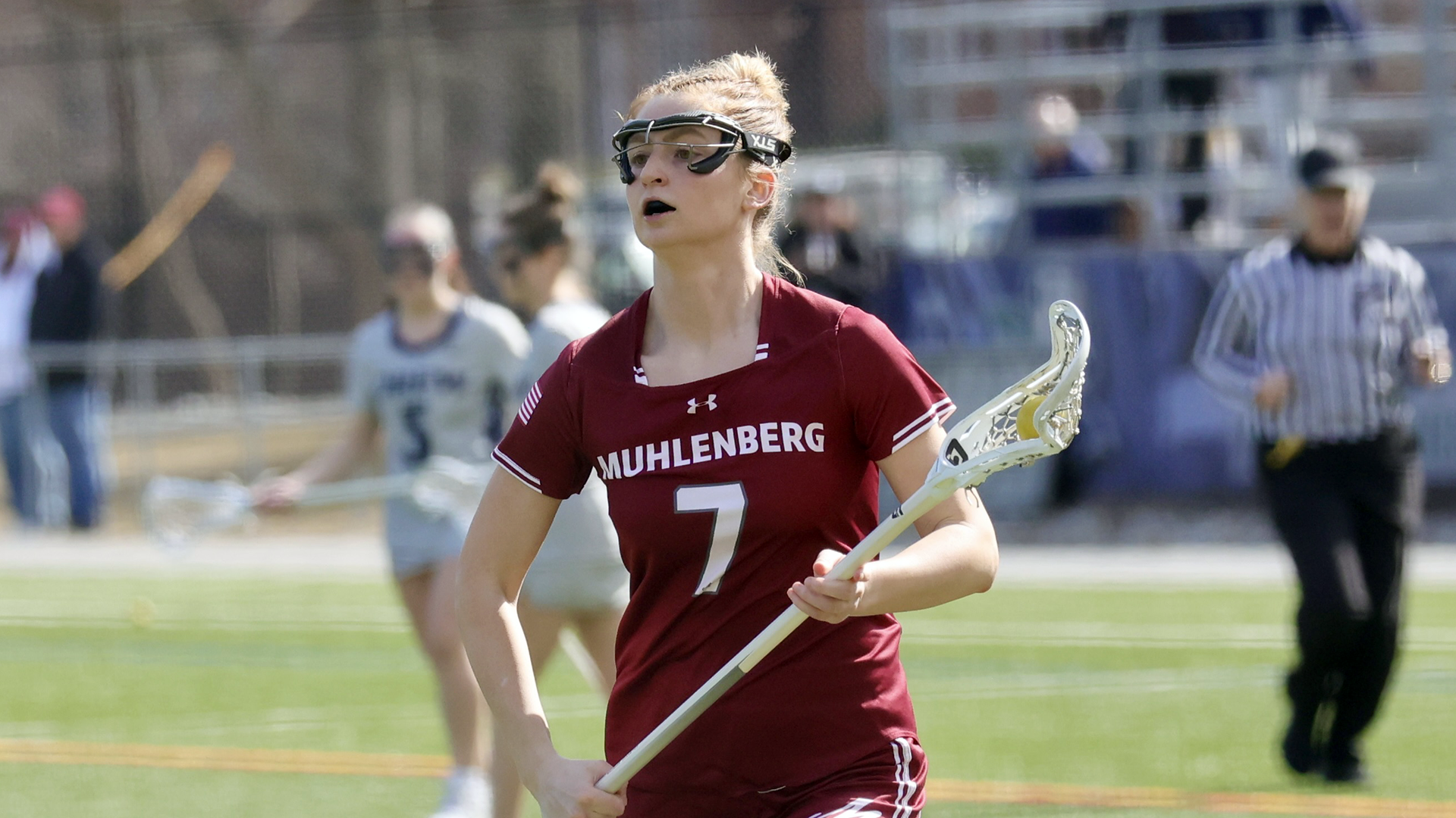 a women's lacrosse player in a red jersey wearing #7 running with the ball in her stick