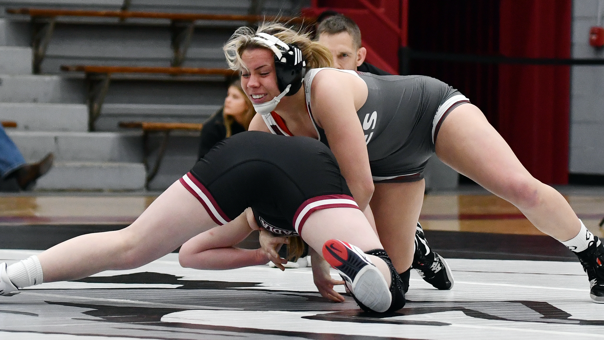 a wrestler in a grey singlet grapples with one in a black singlet as the referee looks on