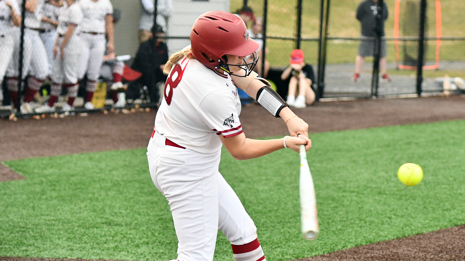 a softball batter in a white jersey and red helmet about to make contact with the ball
